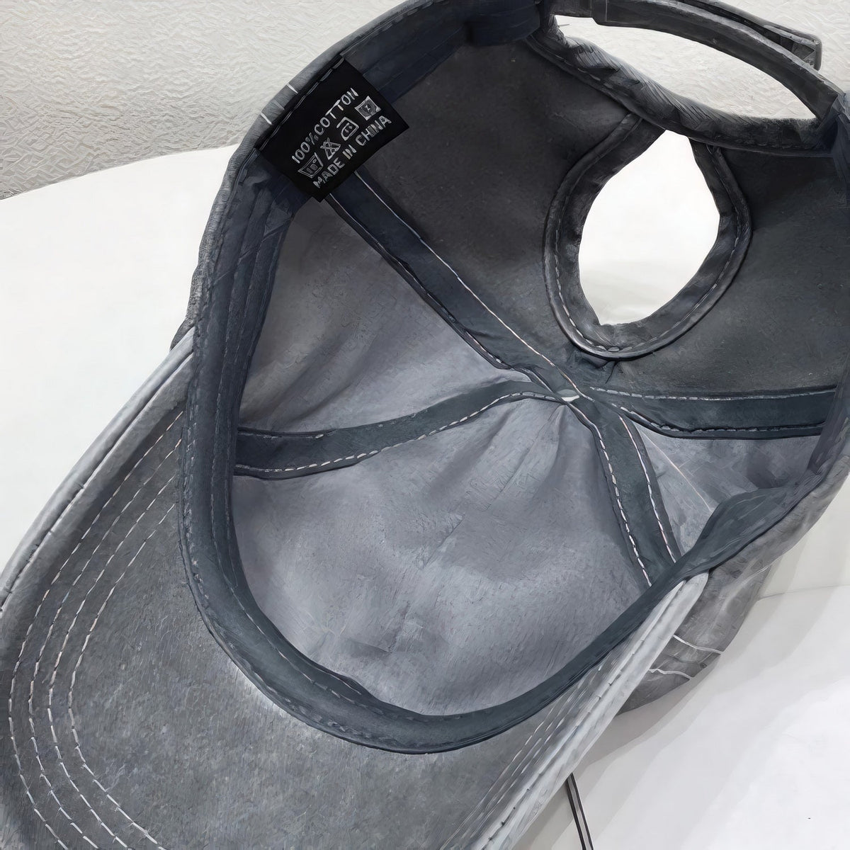 Inside view of a black cotton adjustable baseball cap showing the softly structured six-panel crown, stitched seams, curved brim, and back strap.