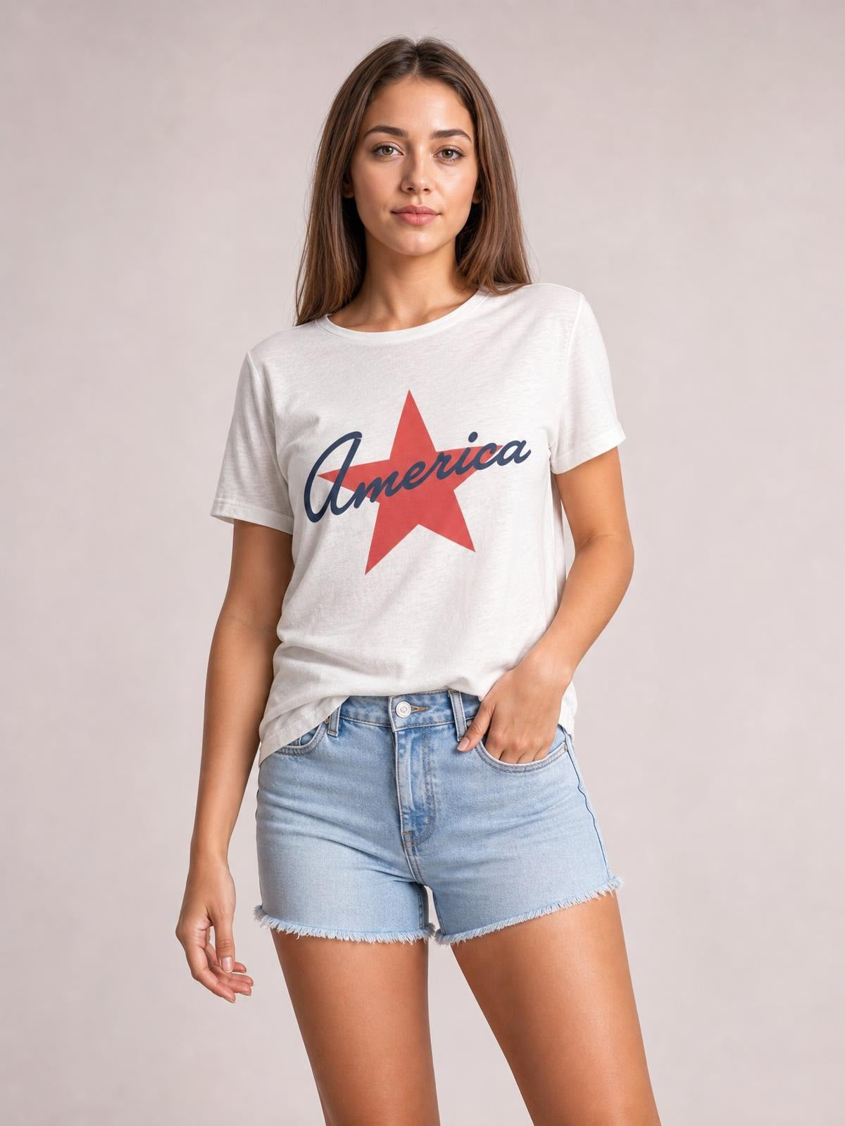 Model poses in a white star graphic T-shirt with a round neck, short sleeves, and relaxed silhouette, paired with light-wash denim shorts.