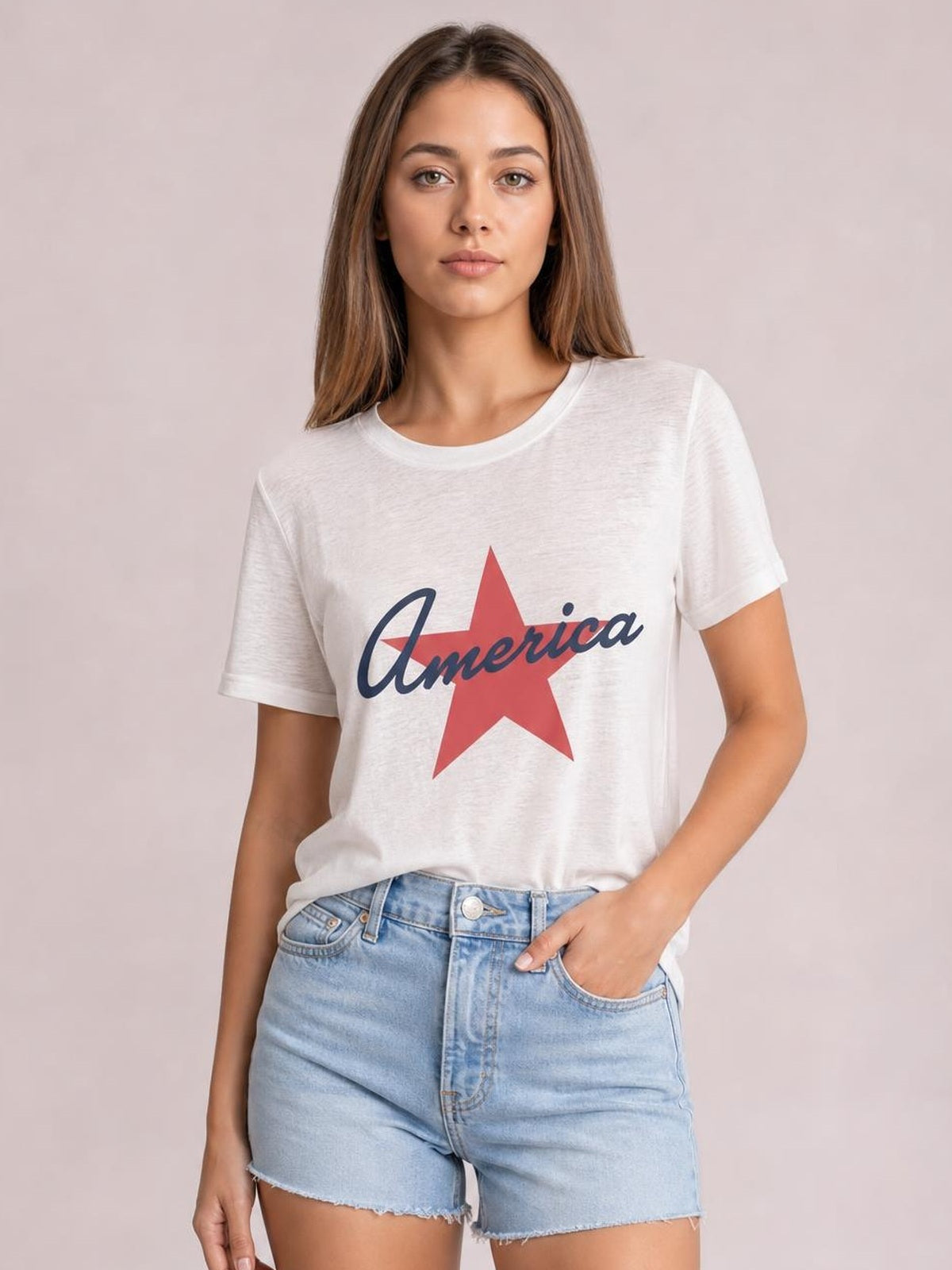 Model wears a white star graphic T-shirt with a round neck, short sleeves, relaxed silhouette, and slightly tucked hem while standing with one hand in her pocket.