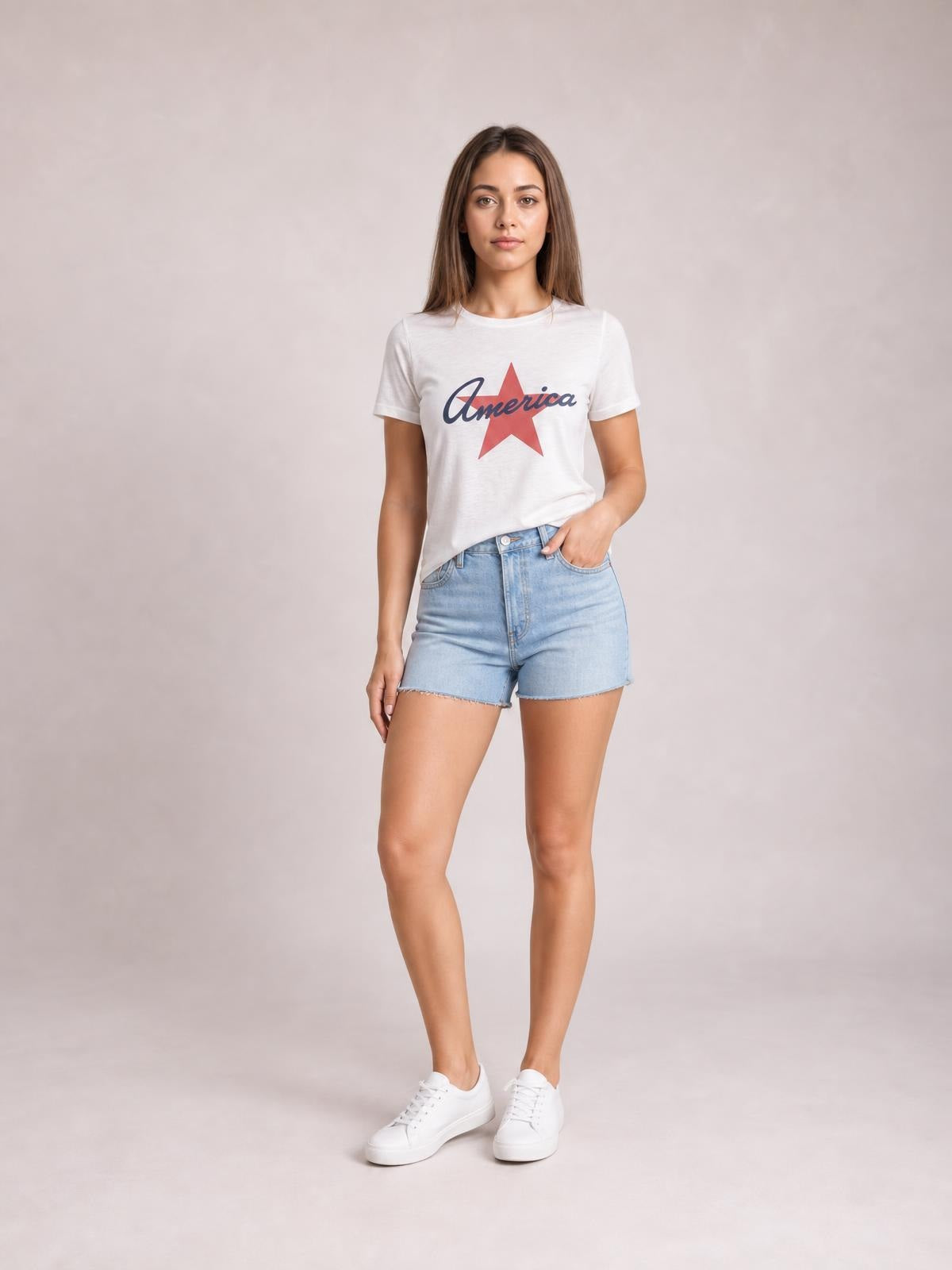 Model wears a white star graphic round neck short sleeve T-shirt with a relaxed silhouette, standing casually with one hand in her denim shorts pocket.