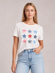 Model wearing a white star round neck short sleeve T-shirt with colorful star print, relaxed silhouette, and one hand tucked into her jeans pocket.