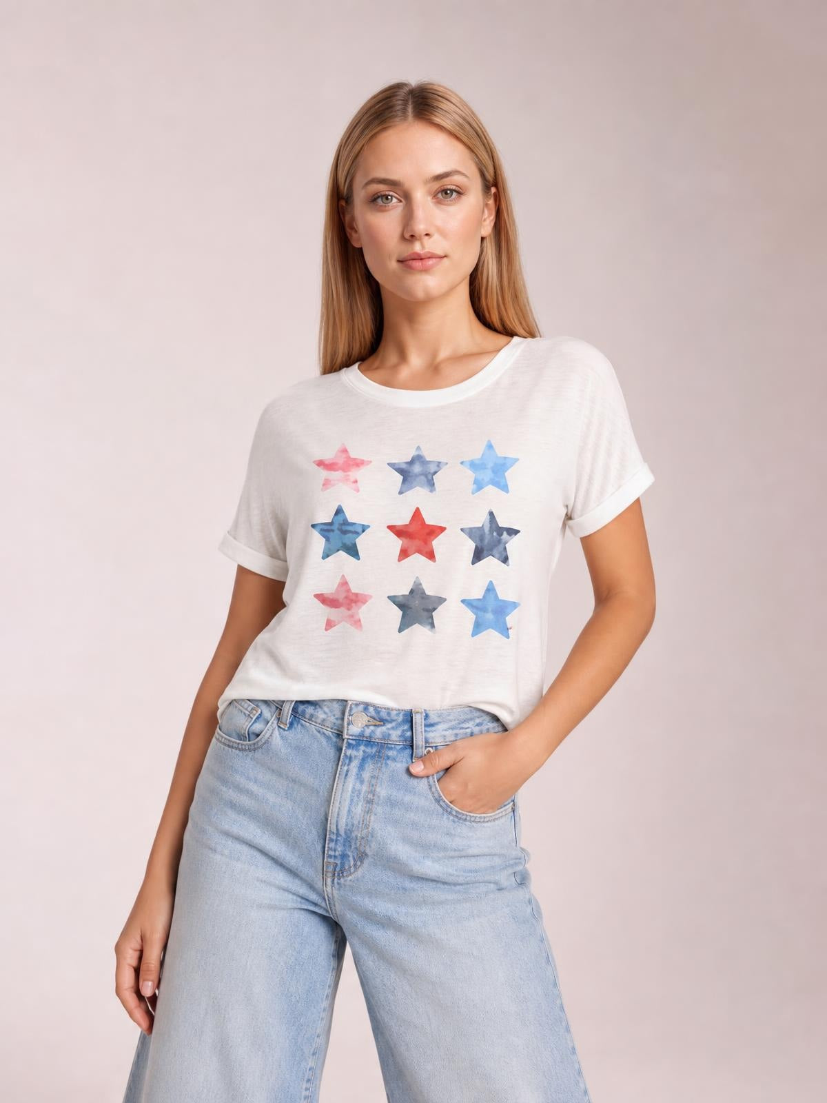 Woman wearing a white star-print round neck short sleeve T-shirt with rolled sleeve cuffs and a relaxed silhouette, posing with one hand in her jeans pocket.