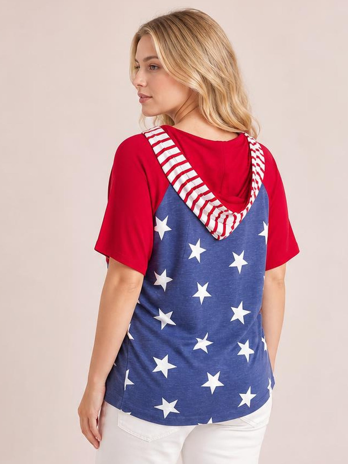 Model shown from the back wears a relaxed stars and stripes print hoodie with a blue starry body, red short sleeves, and a striped hood.