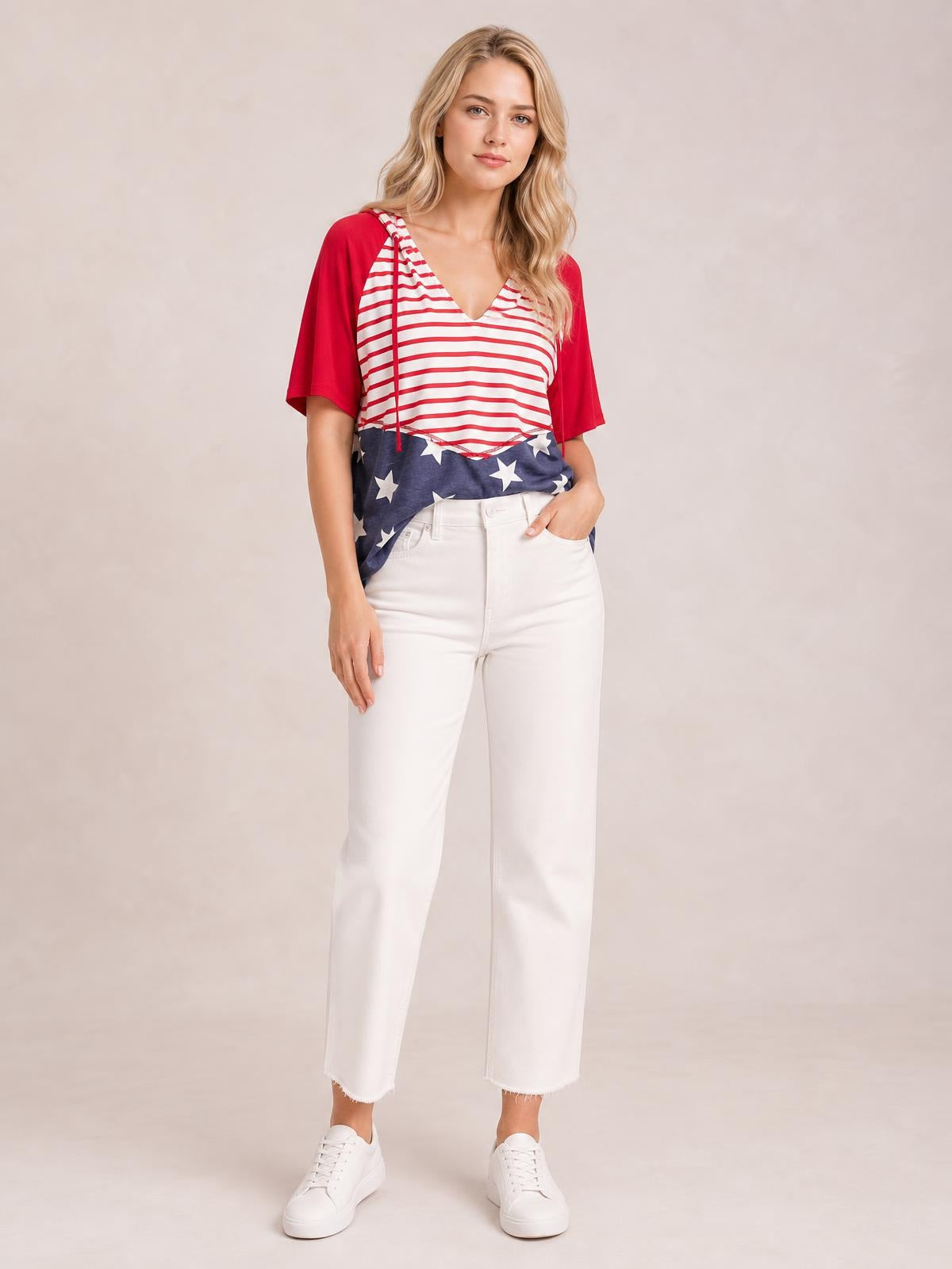A model stands in a relaxed pose wearing a loose stars and stripes print drawstring hoodie with red short sleeves and a V-neckline.