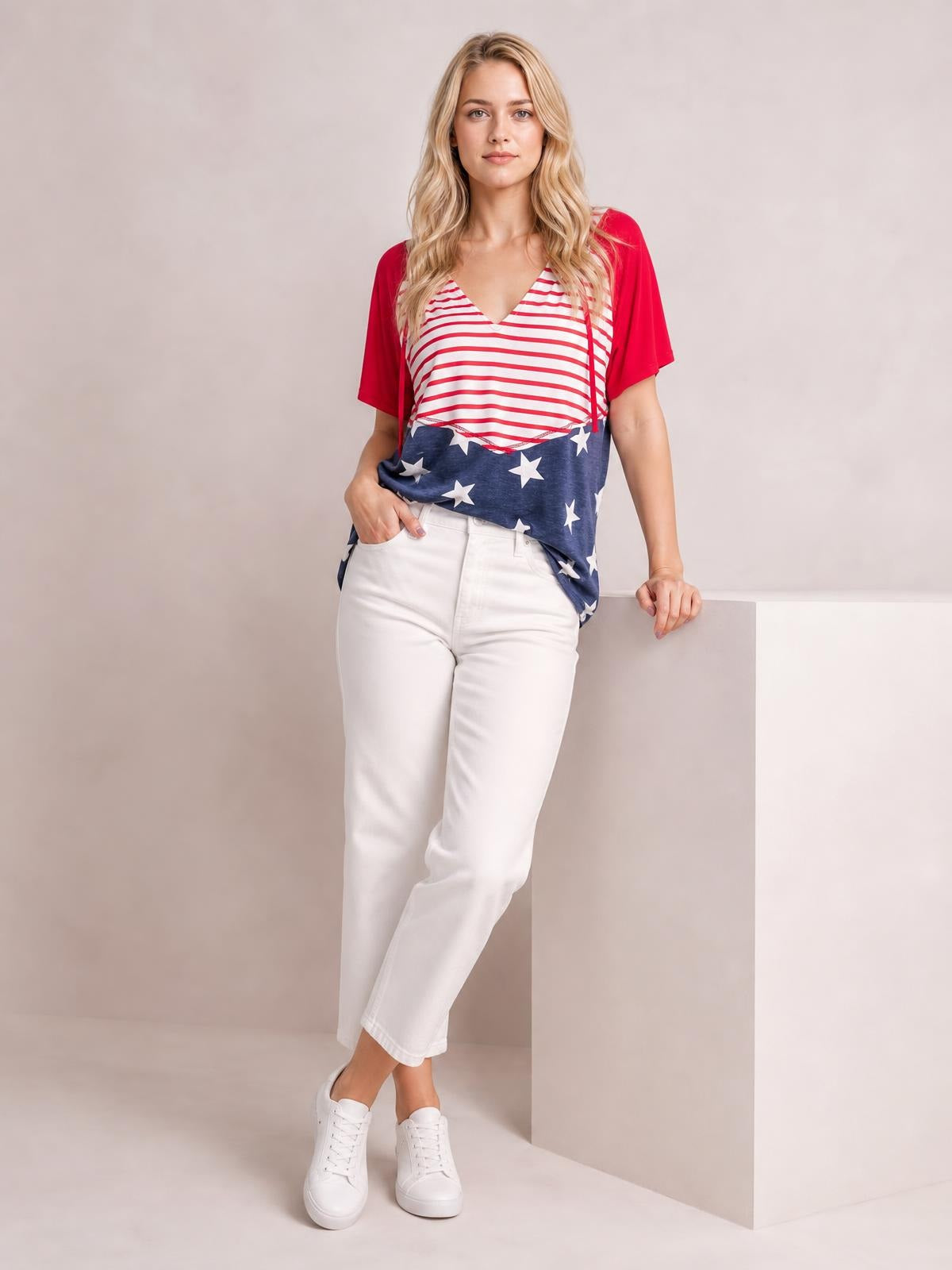 Model wears a loose patriotic drawstring top with red short sleeves, a V-neck, red-and-white stripes, and a navy star-print lower panel.