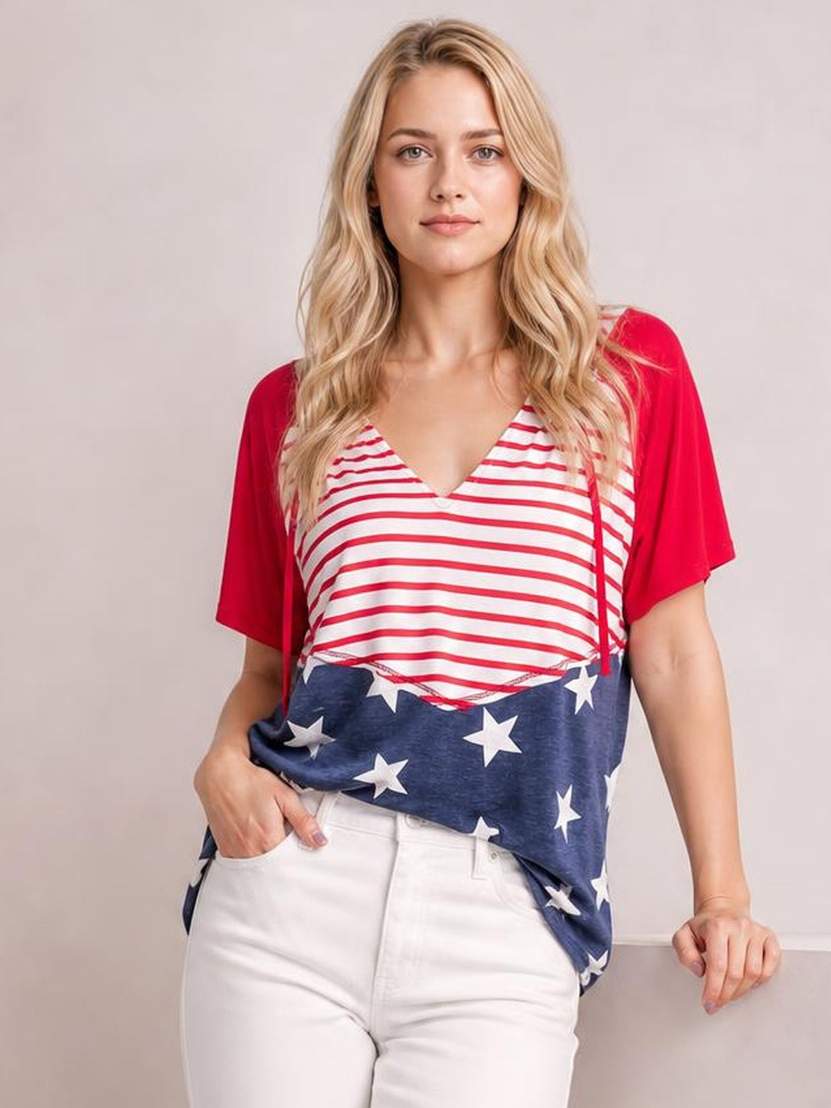 Model wears a red, white, and navy stars and stripes print drawstring shirt with a V-neck, short sleeves, and a relaxed tunic silhouette.