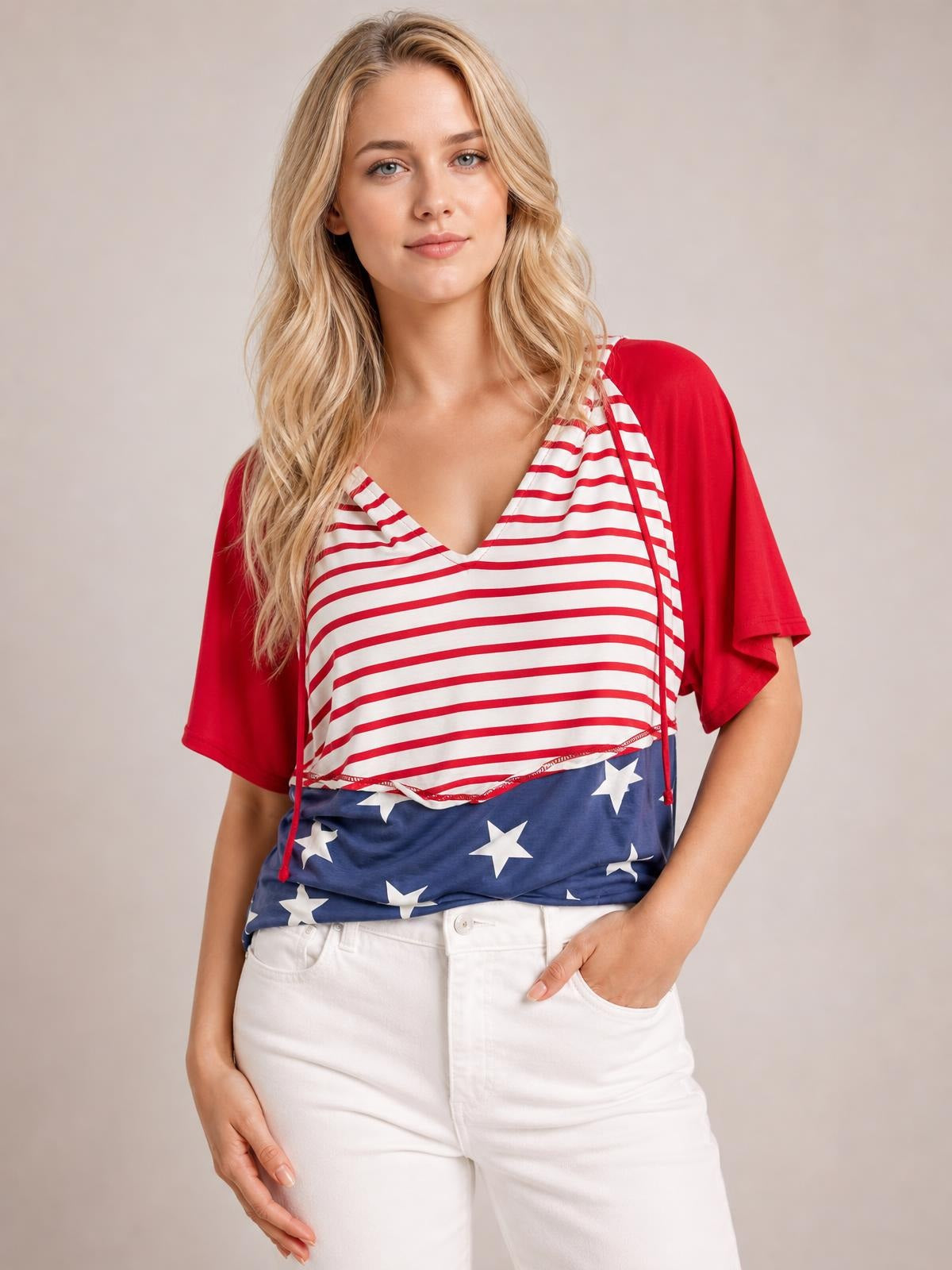 A model poses in a patriotic stars and stripes drawstring hoodie with red short sleeves, a V-neck, striped bodice, and blue star-print hem.