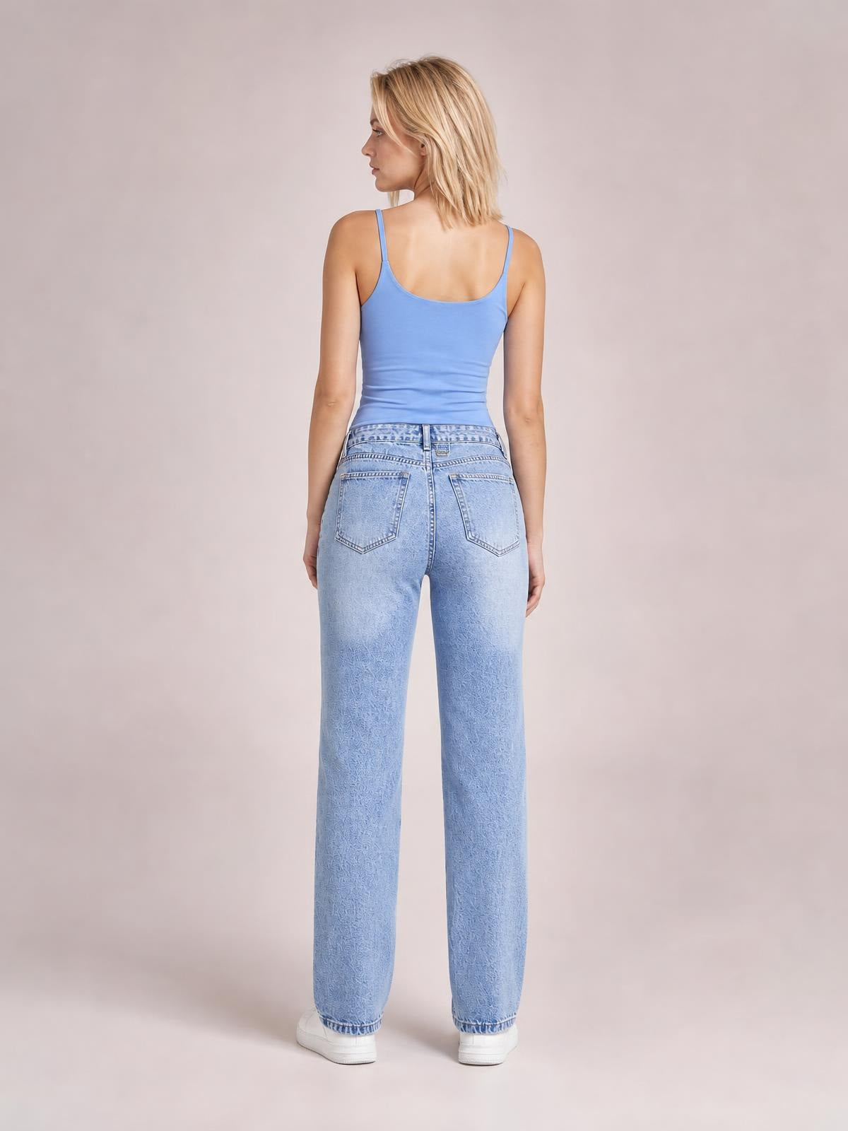 A model stands facing away in light-wash straight jeans with a buttoned waistband, belt loops, and two stitched back pockets.