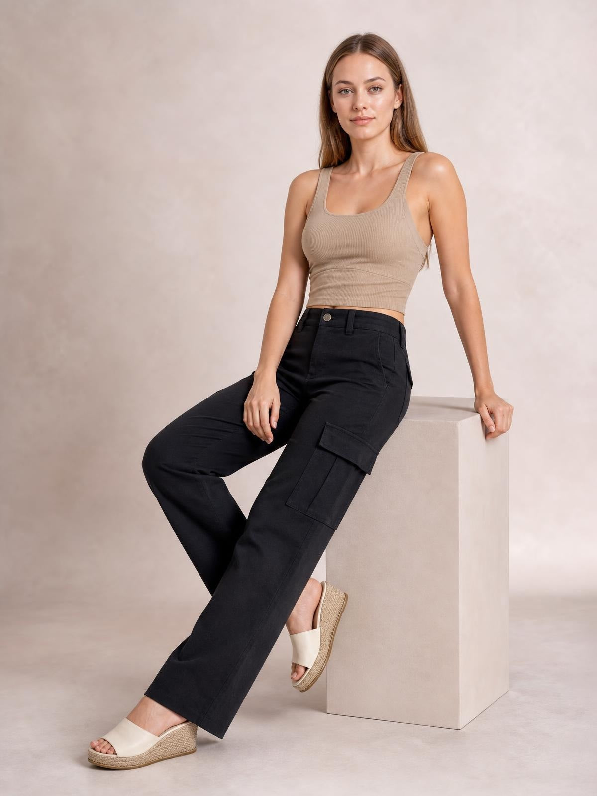 Model seated in black straight-leg cargo pants with a structured waistband, belt loops, and flap cargo pockets, showing the relaxed silhouette and opaque construction.