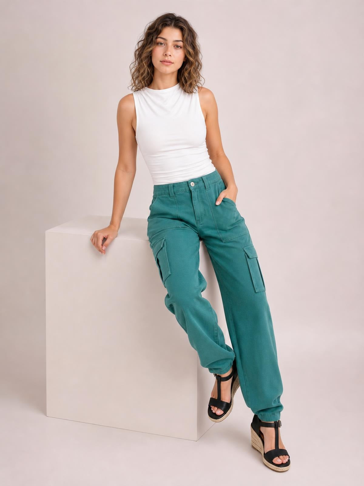 Model poses in teal straight leg cargo pants with belt loops, button closure, and multiple utility pockets, one hand tucked into a pocket.