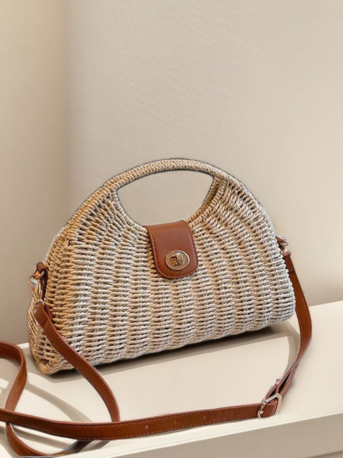 Medium straw woven crossbody bag with a rounded structured silhouette, adjustable brown strap, and leather-look flap with metal turn-lock closure.