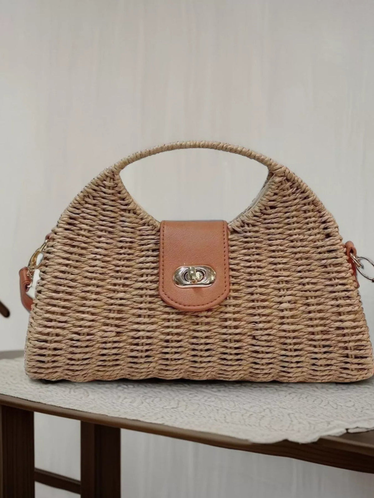 A medium straw-woven crossbody bag features a structured tan silhouette, adjustable strap, leather flap closure, and polished silver turn-lock hardware.