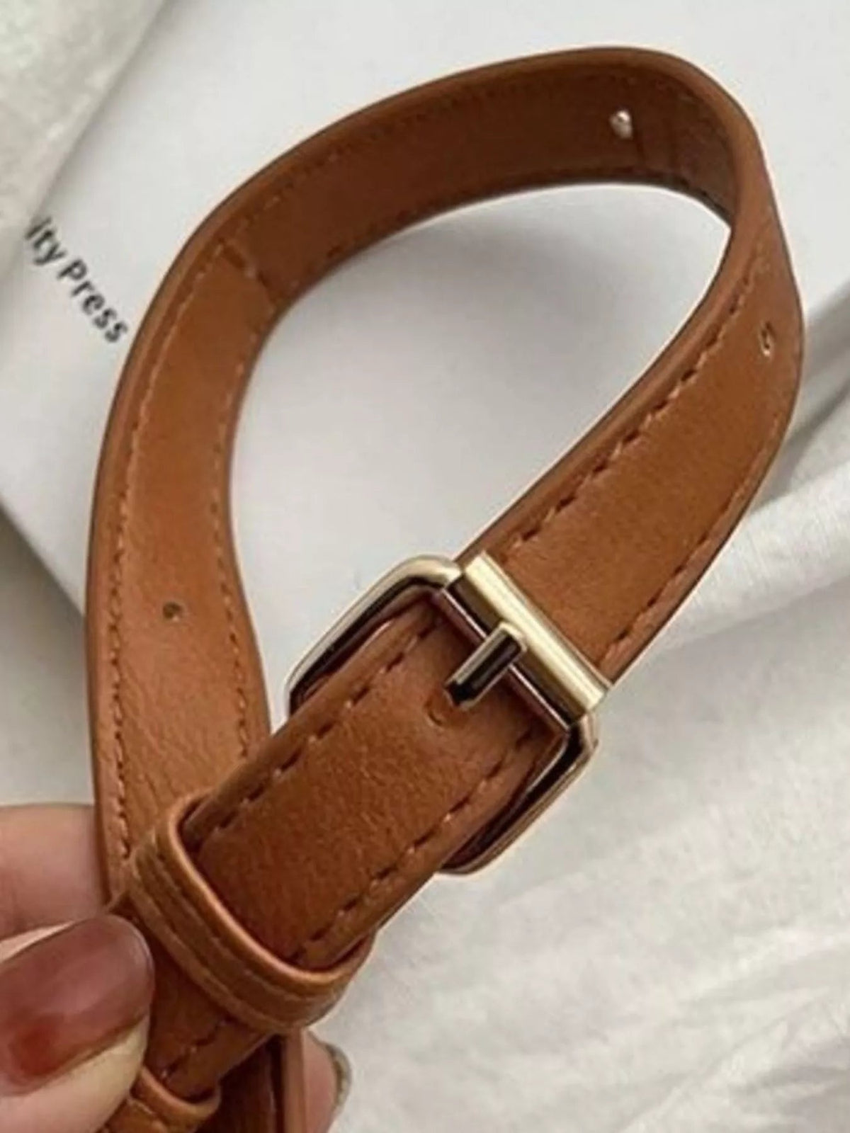 Close-up of the medium crossbody bag’s adjustable brown strap, showing stitched edges, punched adjustment holes, and a metal buckle.