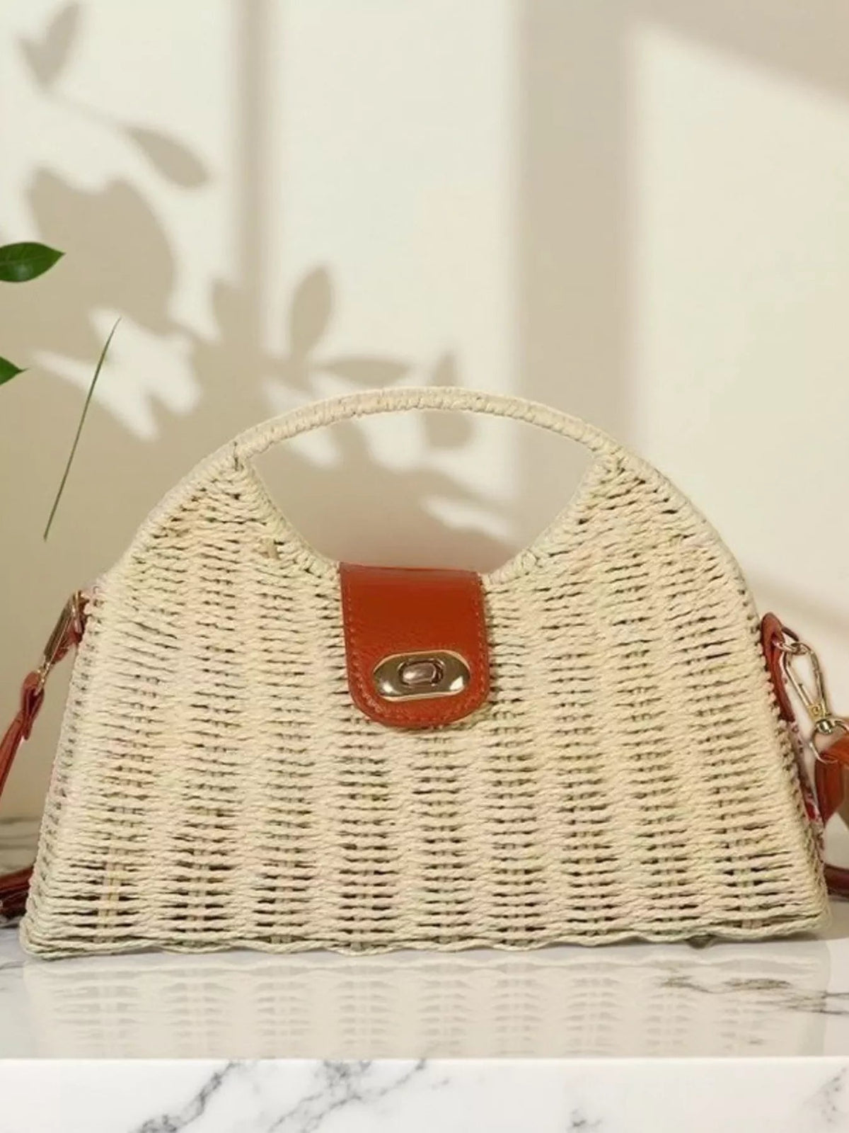 Medium straw woven crossbody bag with a structured trapezoid silhouette, adjustable side strap, brown leather-look flap, and gold-tone turn-lock closure.