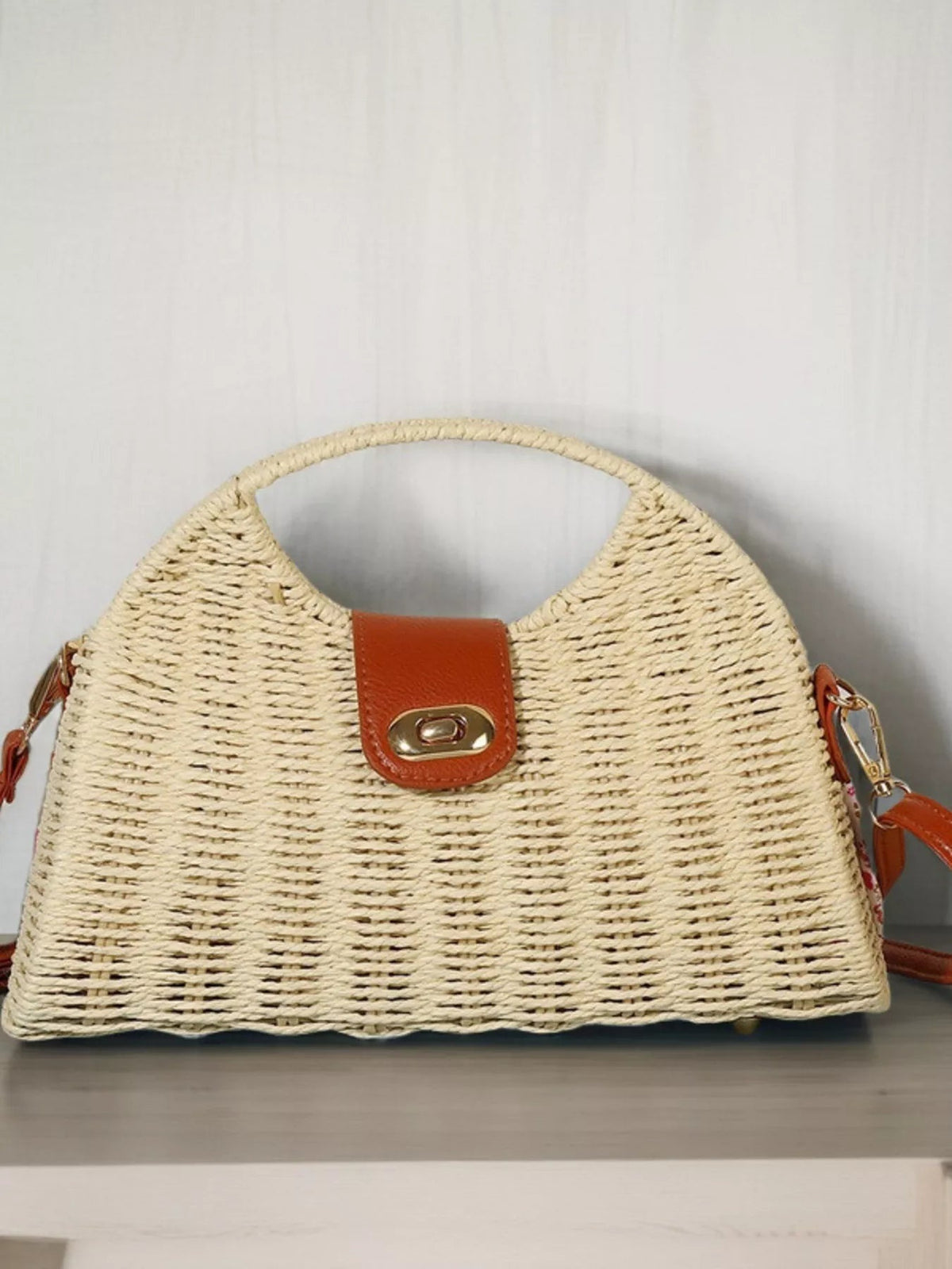 Medium straw woven crossbody bag with a structured trapezoid silhouette, rounded top handle, adjustable brown strap, and leather flap with gold-tone clasp.