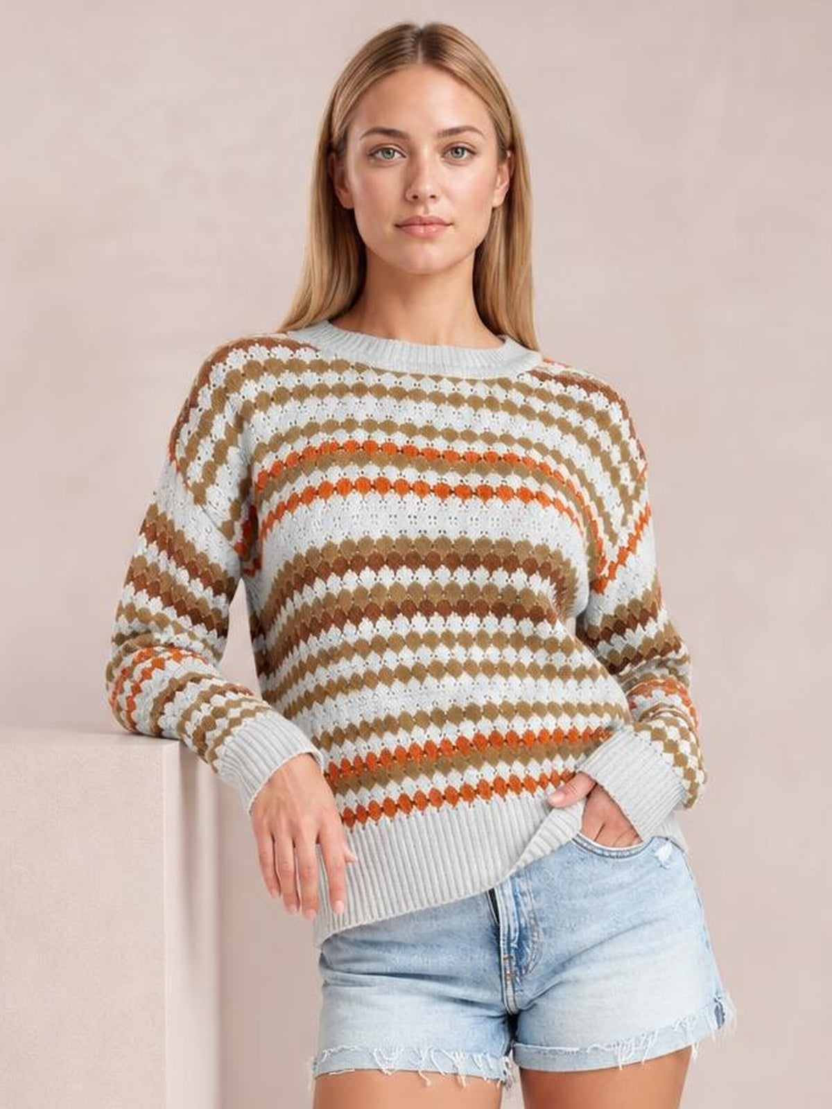 Model wears a light gray striped eyelet-patterned drop-shoulder sweater with brown and orange accents, ribbed trim, and a relaxed silhouette.