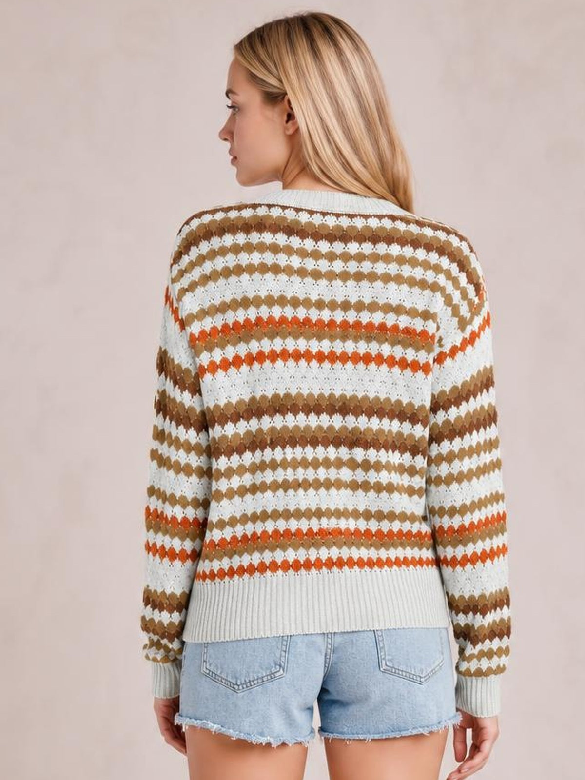 Model shown from the back wearing a cream drop-shoulder sweater with brown and orange horizontal stripe eyelet pattern, ribbed cuffs and hem.