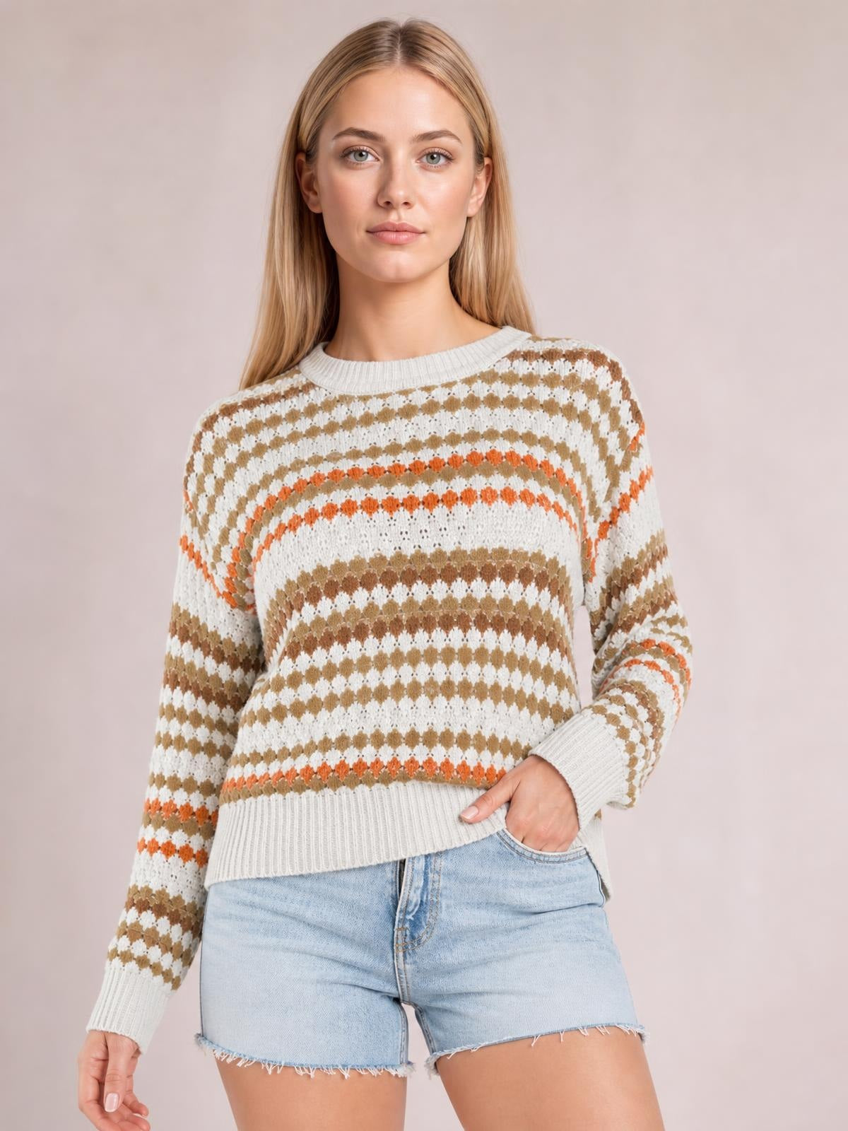 Model wears a relaxed drop-shoulder sweater with cream, tan, and orange striped eyelet pattern, ribbed crew neckline, cuffs, and hem.