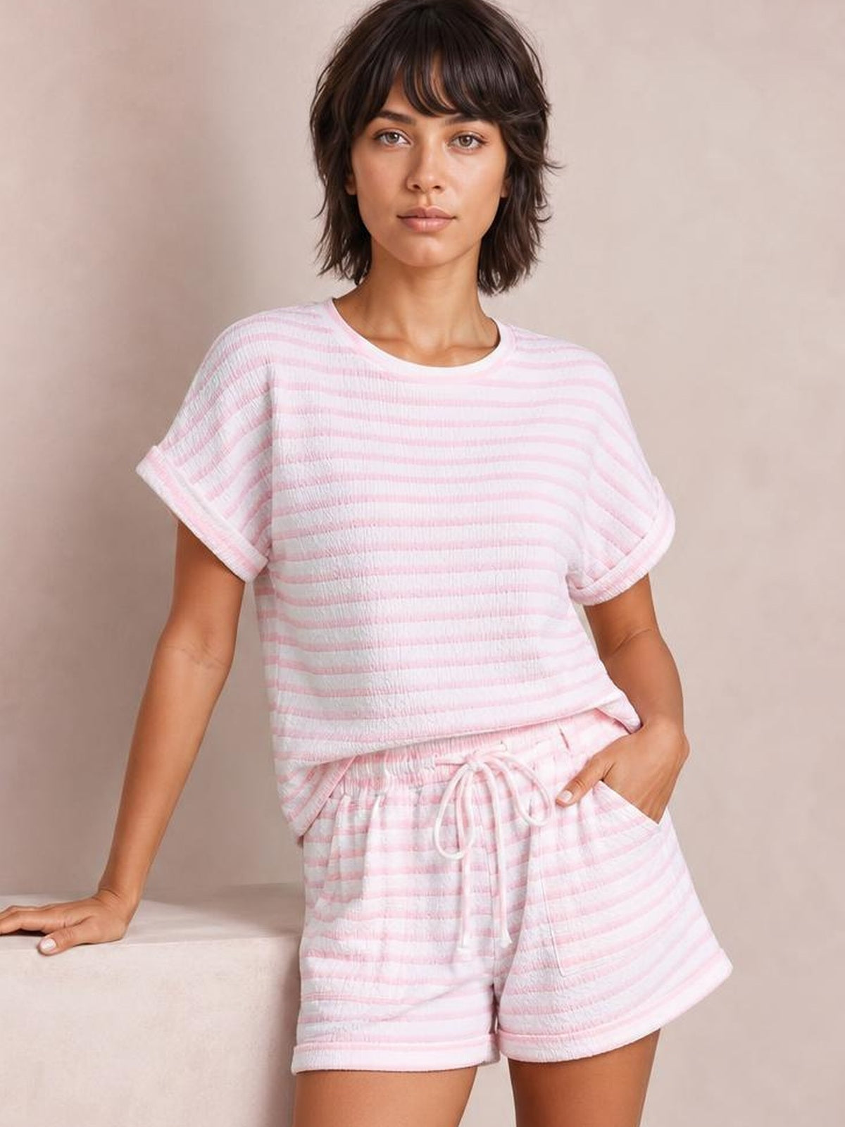 Model poses in a pink-and-white striped knitted short sleeve top and matching drawstring shorts set with rolled cuffs and relaxed silhouette.
