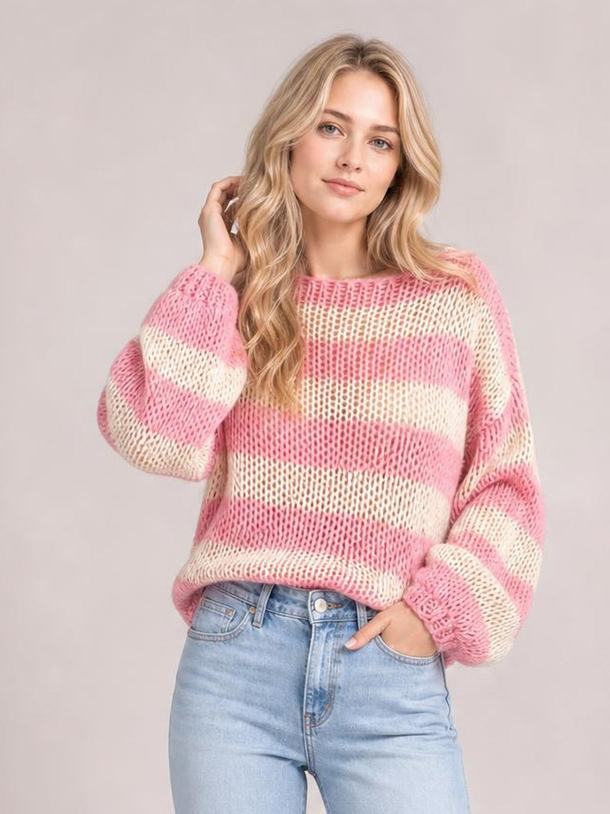 Model poses in a pink-and-cream striped boat neck long sleeve sweater with a relaxed loose-knit silhouette and oversized sleeves.