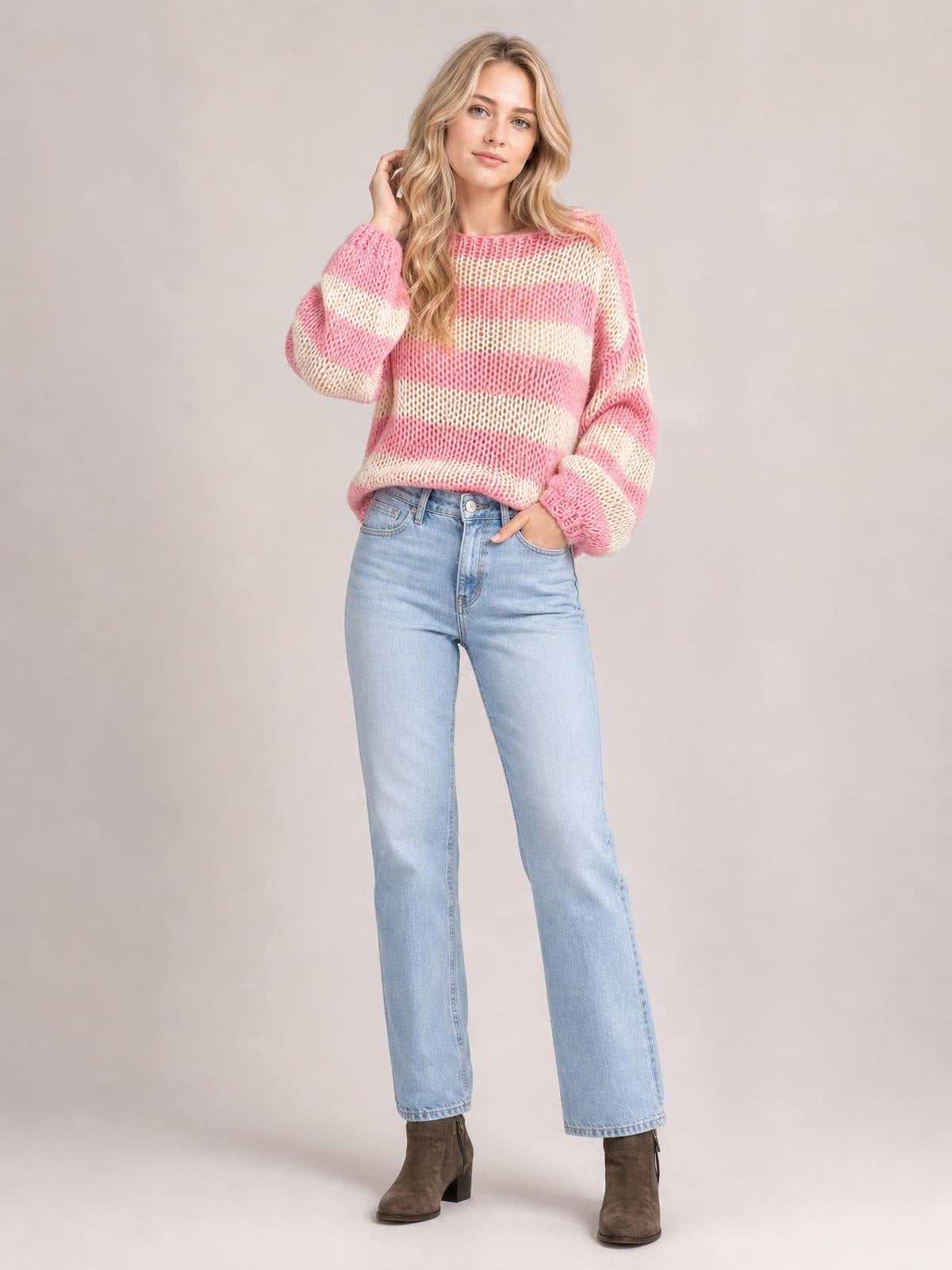 A model poses in a relaxed pink and cream striped boat neck sweater with long sleeves, open-knit construction, and a slightly loose silhouette.