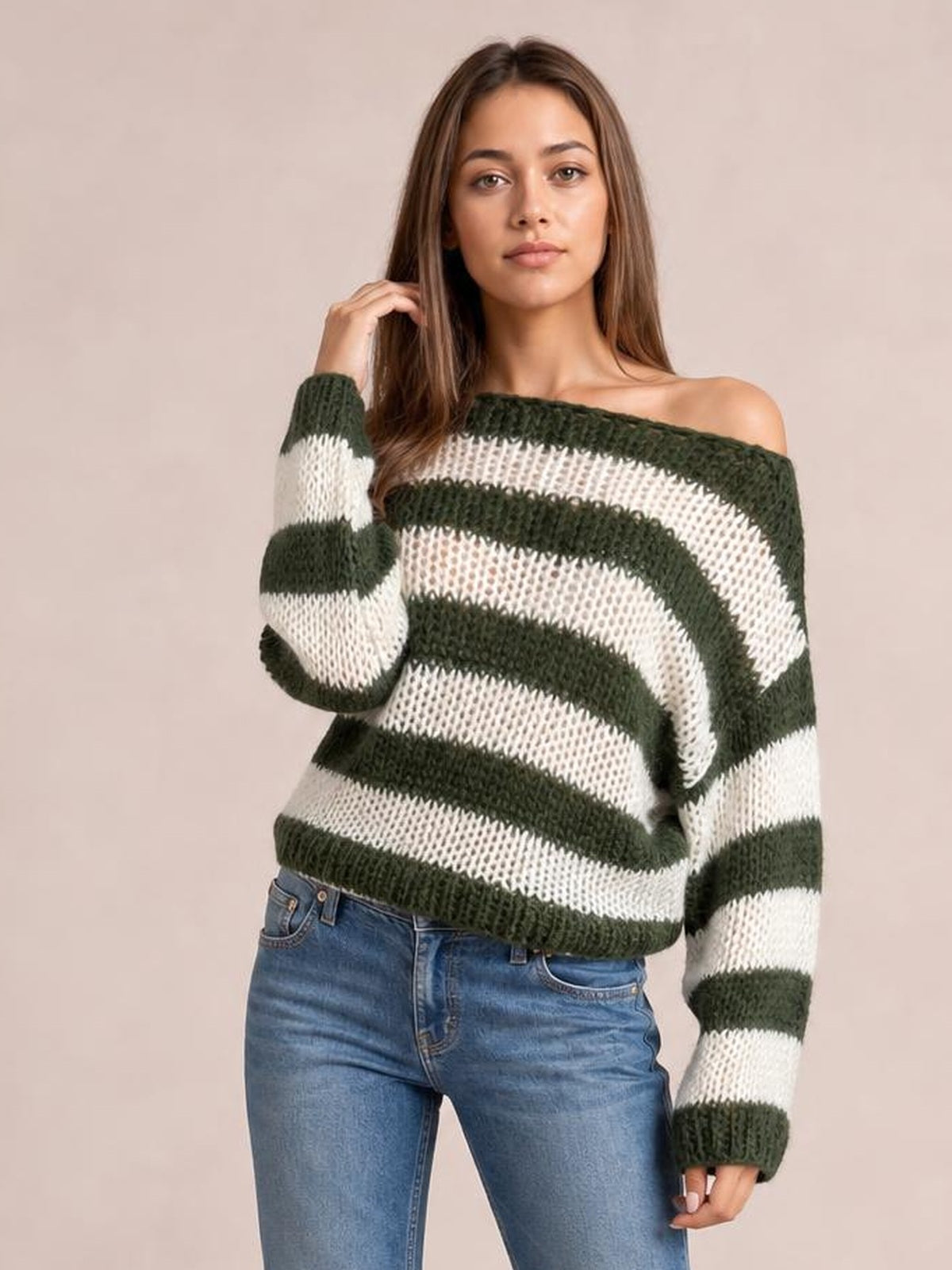 Model poses in a striped boat neck long sleeve sweater with dark green and white bands, a relaxed silhouette, wide ribbed cuffs, and an exposed shoulder.