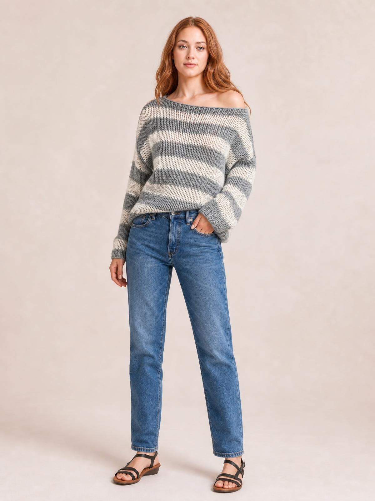 Model poses in a gray and cream striped boat neck long sleeve sweater with a relaxed silhouette and ribbed cuffs.