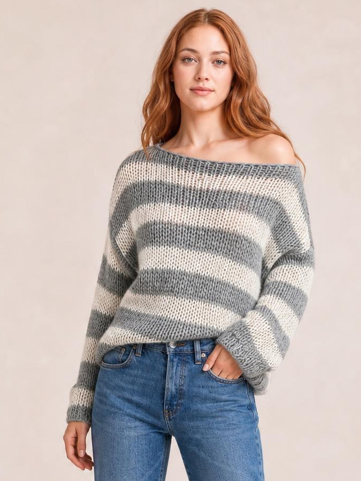 A model wears a gray and cream striped boat neck long sleeve sweater with a relaxed silhouette and ribbed cuffs, posing with one hand in her jeans pocket.