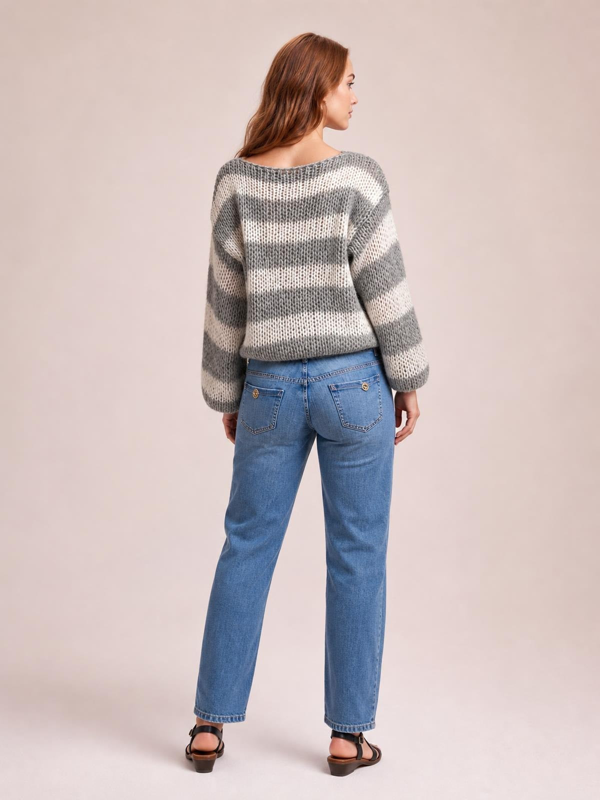 Model shown from the back wearing a gray and white striped boat neck long sleeve sweater with a relaxed silhouette and ribbed knit construction.