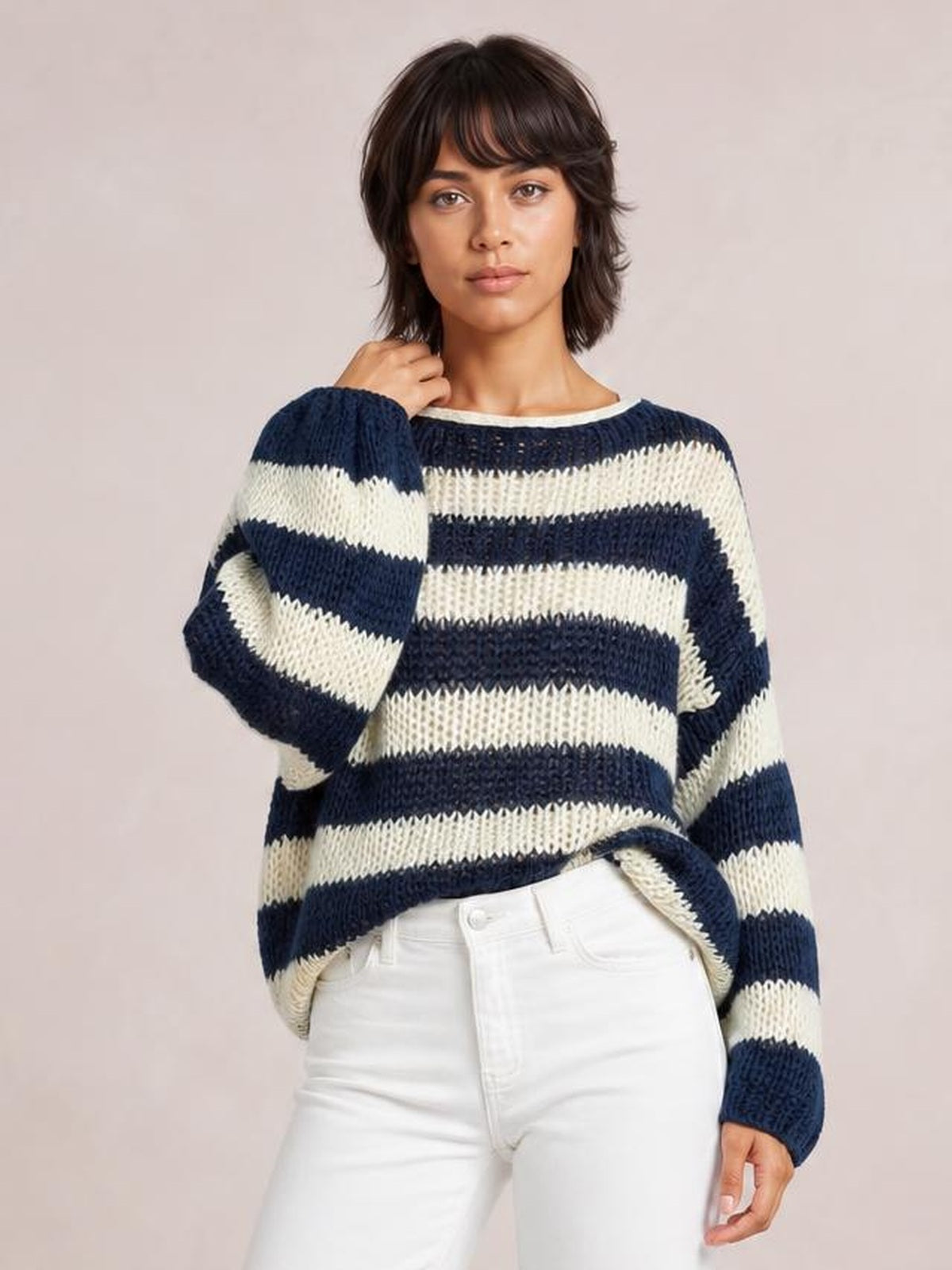 Model poses in a relaxed striped boat neck long sleeve sweater with navy and cream bands, a loose silhouette, and chunky knit construction.