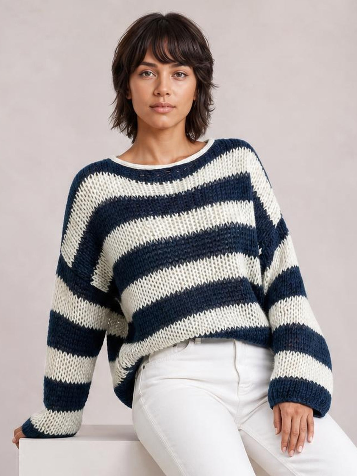 Model wears a navy and cream striped boat neck long sleeve sweater with a relaxed oversized silhouette and chunky knit texture.