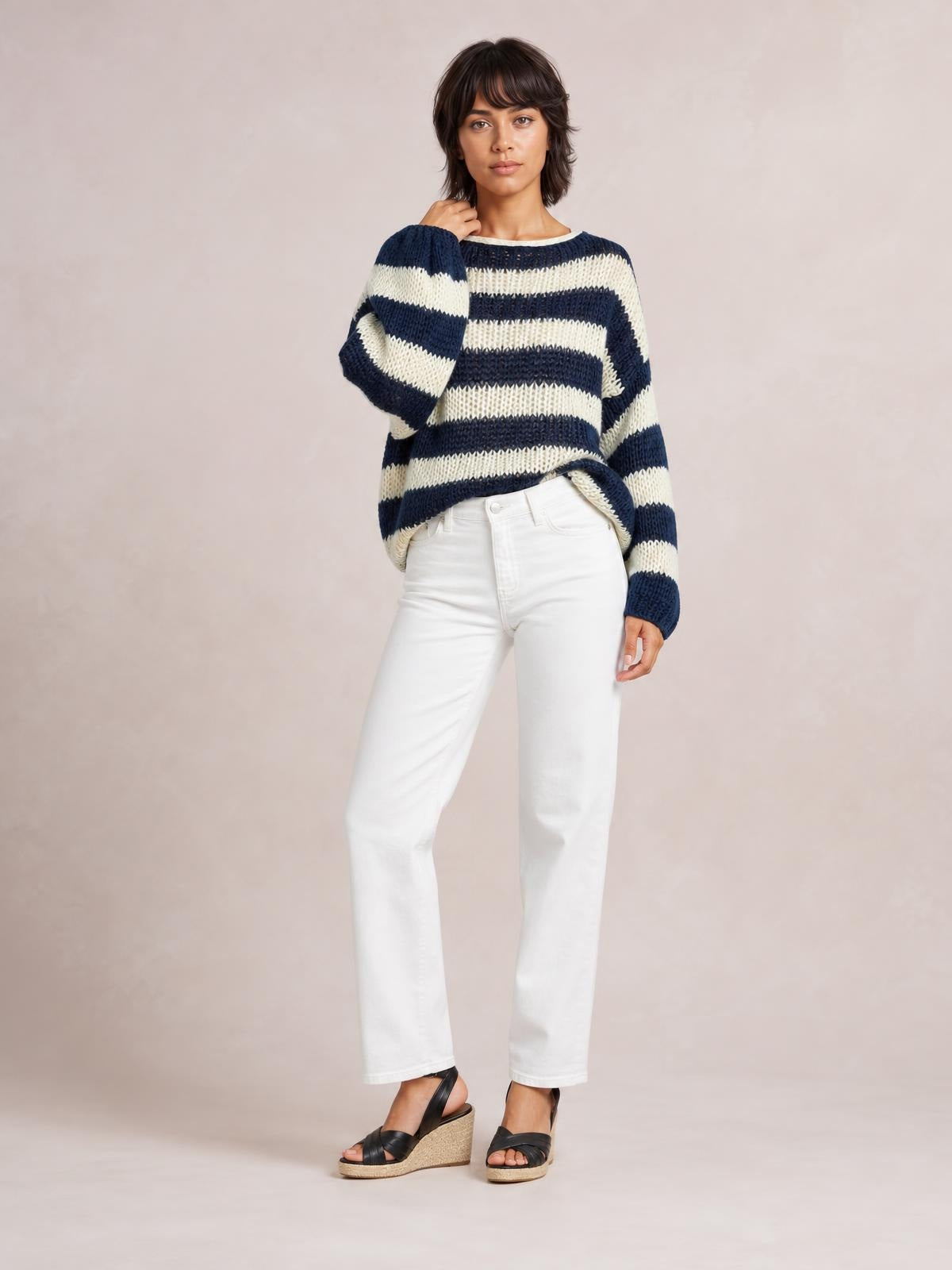 Model poses in a navy and ivory striped boat neck long sleeve sweater with a relaxed silhouette, ribbed cuffs, and a slightly curved hem.