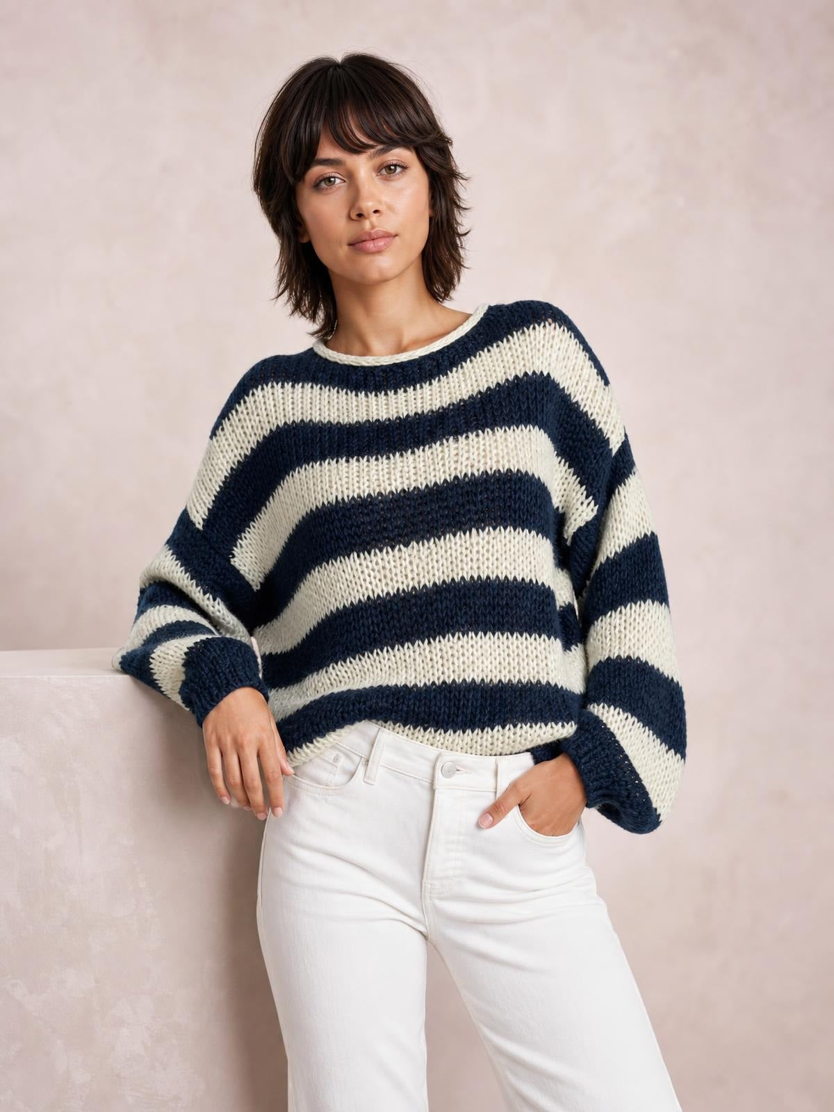 Model poses with one hand in her pocket wearing a navy and ivory striped boat-neck long-sleeve sweater with a relaxed knit silhouette and ribbed cuffs.