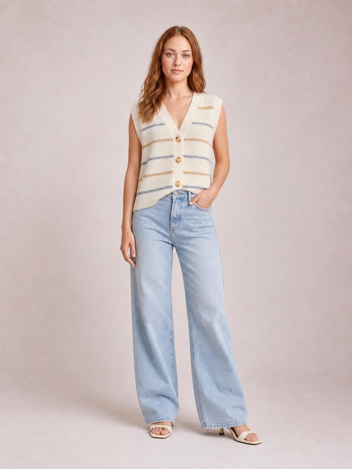 Model wears a cream striped button-down sweater vest with a V-neck, sleeveless silhouette, ribbed trim, and three front buttons.