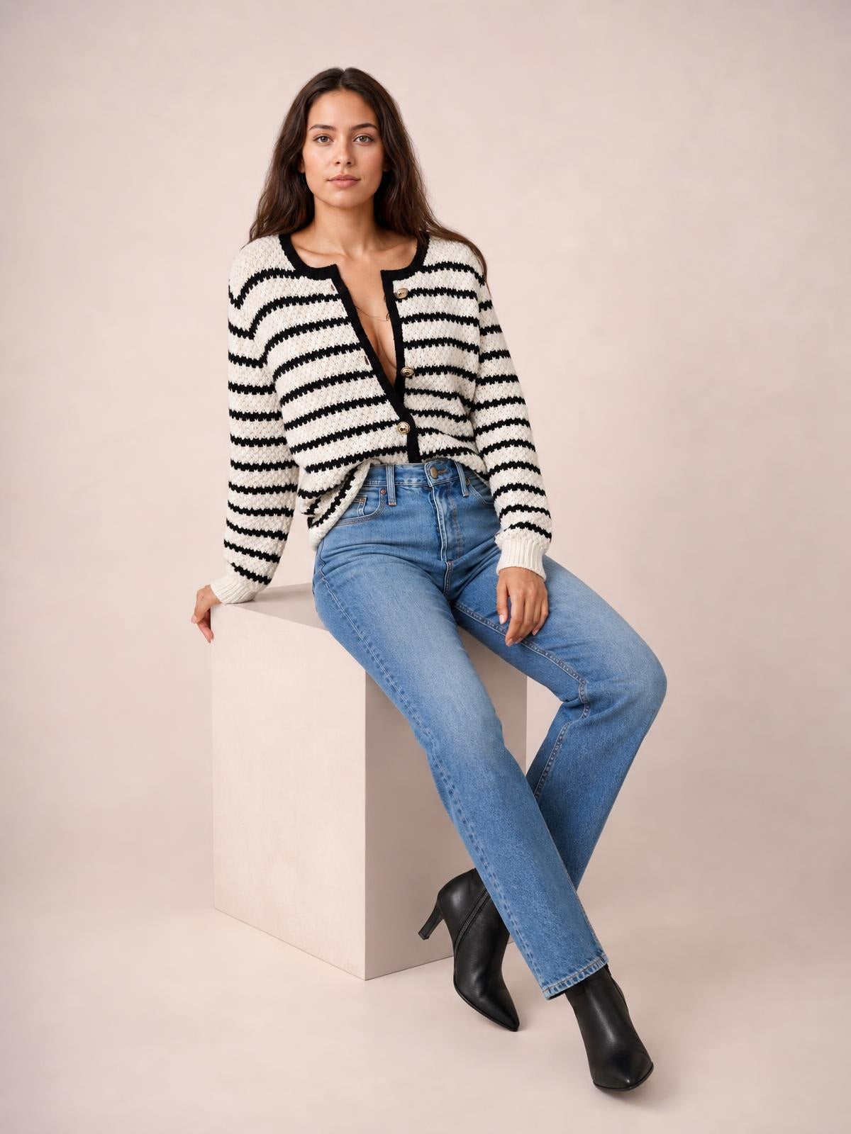 Model seated and wearing a black-and-white striped button-up cardigan with long sleeves, a cropped silhouette, ribbed trim, and front buttons.
