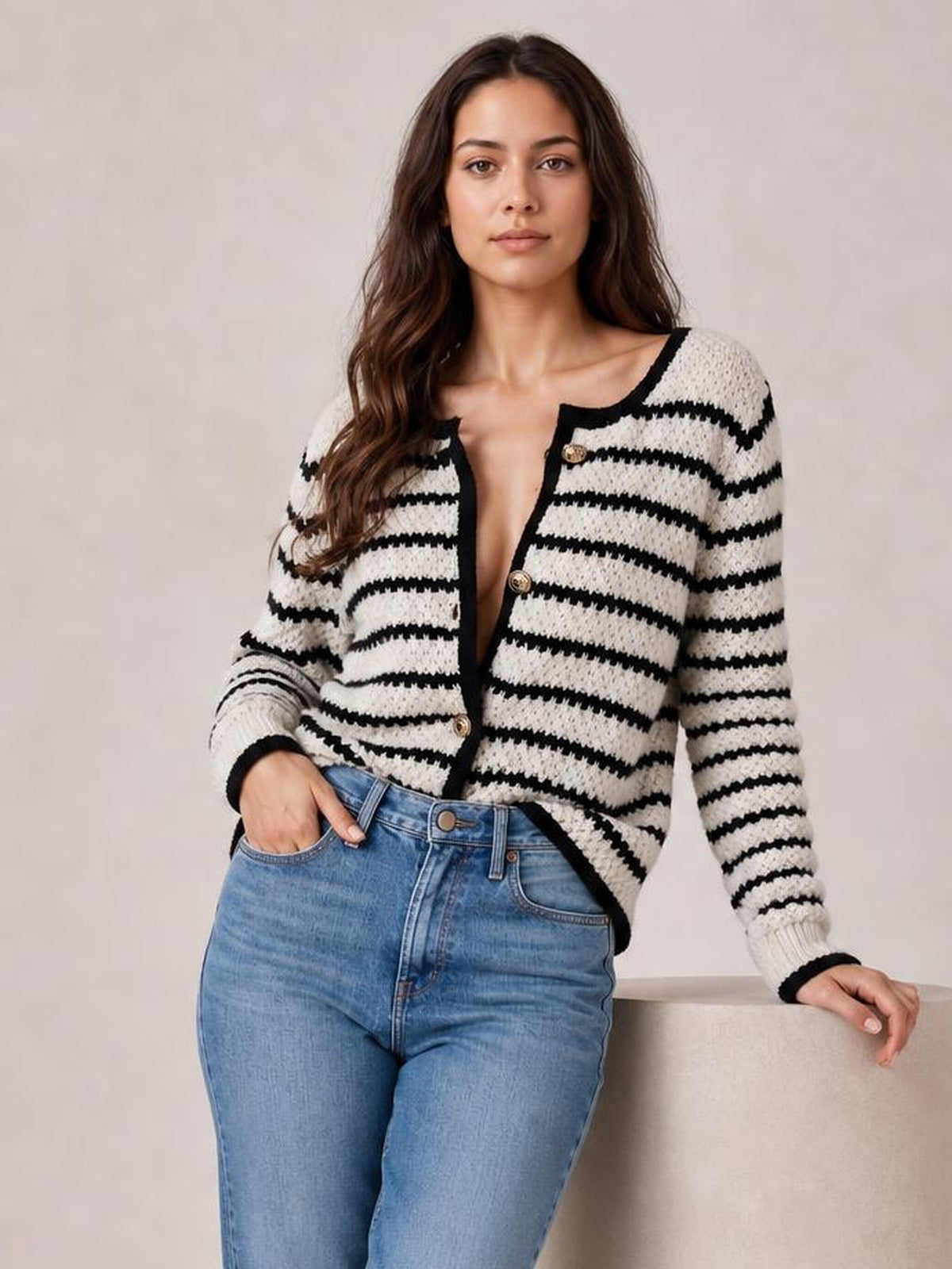 Model wearing a cream and black striped button-up long sleeve cardigan with contrasting trim and a fitted silhouette, leaning with one hand in her jeans pocket.