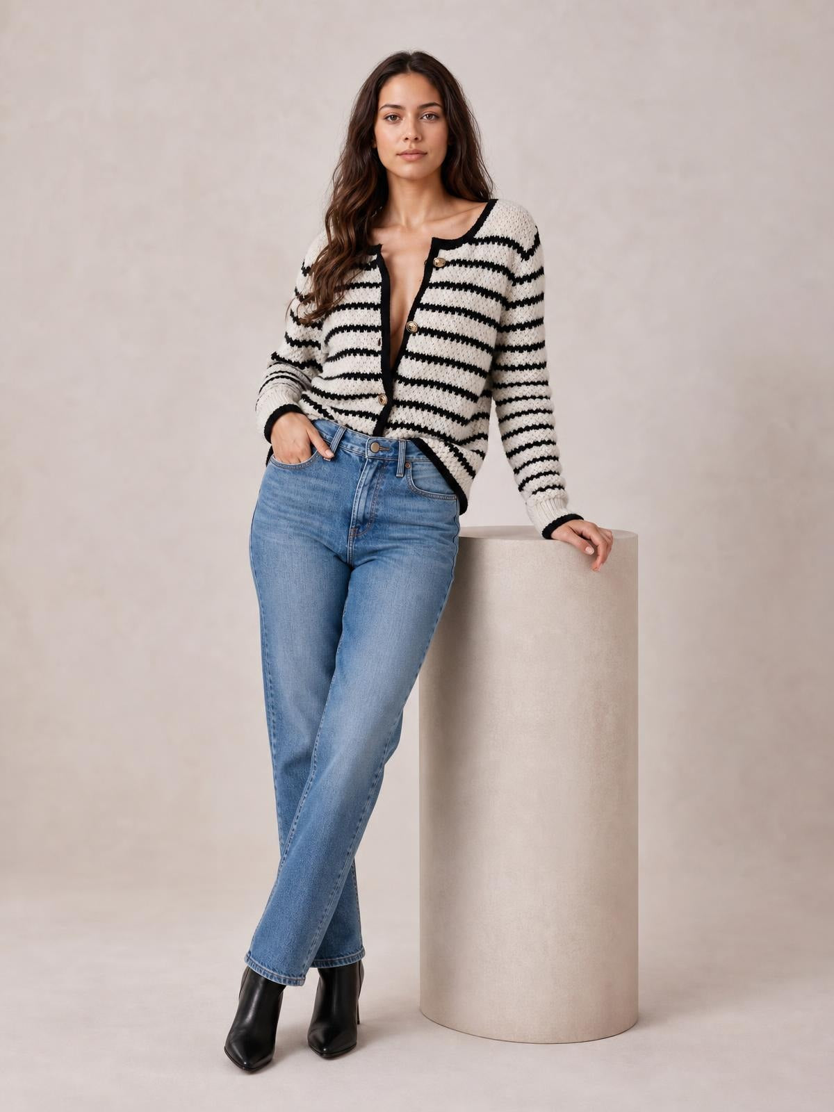 Model wearing a black and white striped button-up long sleeve cardigan with a relaxed silhouette, contrast trim, and front buttons while leaning against a pedestal.