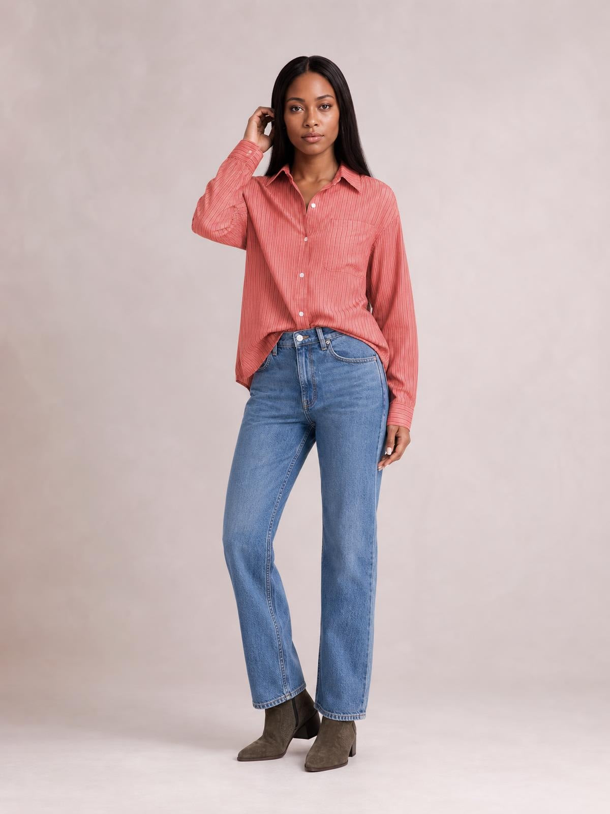 Model poses in a coral striped button-up long sleeve shirt with a collared neckline, front buttons, and buttoned chest pockets in a relaxed silhouette.