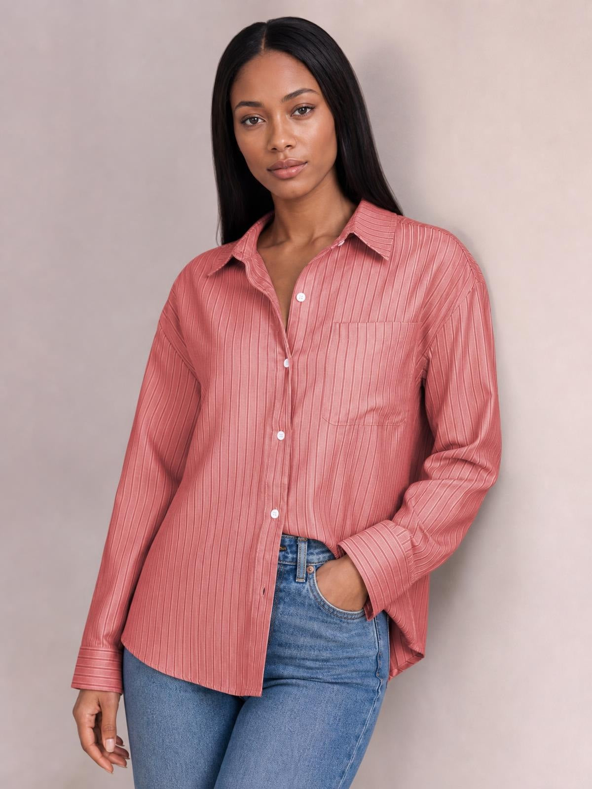 Model poses in a pink striped button-up long sleeve shirt with a pointed collar, white buttons, chest pocket, and relaxed silhouette.