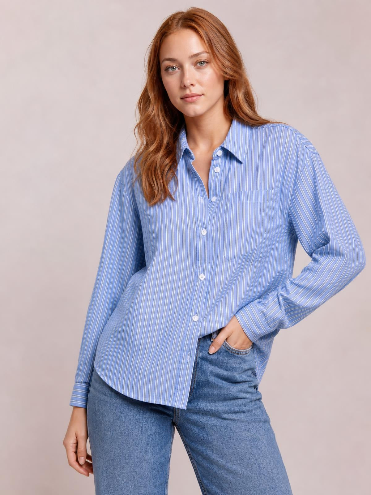 Model wearing a blue striped button-up long-sleeve shirt with a collared, relaxed silhouette, front buttons, and a visible chest pocket, posing with one hand in her jeans pocket.