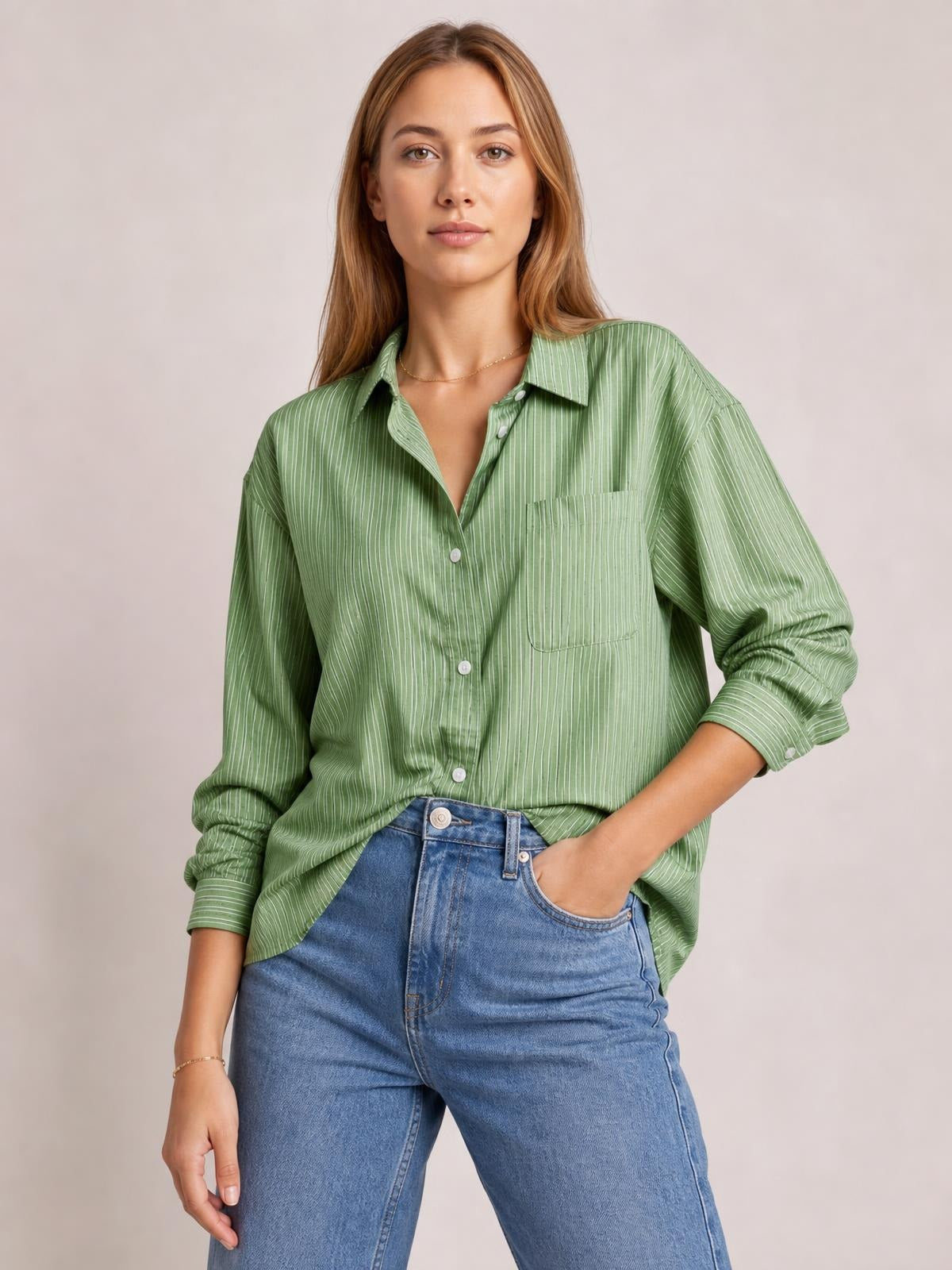 Model in a relaxed pose wears a sage green striped button-up long sleeve shirt with a collared neckline, front buttons, buttoned chest pocket, and loose silhouette.