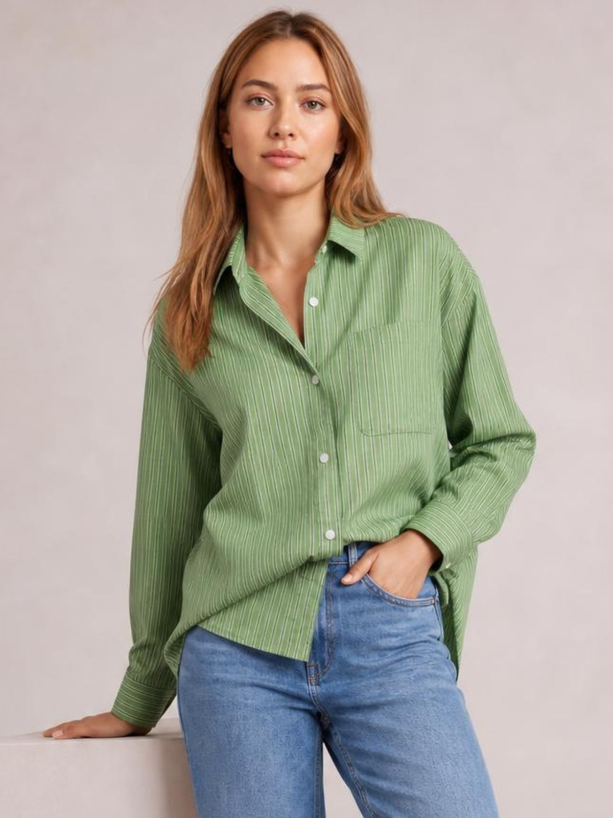Model wears a green striped button-up long-sleeve shirt with a collared, relaxed silhouette, white buttons, and a visible chest pocket.