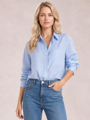 Model wearing a light blue striped button-up long sleeve shirt with a collared neckline, front buttons, chest pocket, relaxed silhouette, and rolled sleeves.