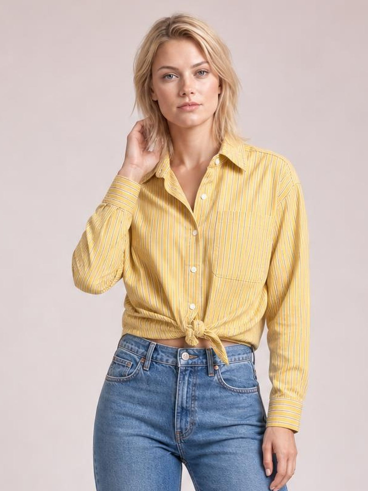 Model wearing a yellow striped button-up long-sleeve shirt with a pointed collar, front buttons, chest pocket, relaxed silhouette, and tied hem.