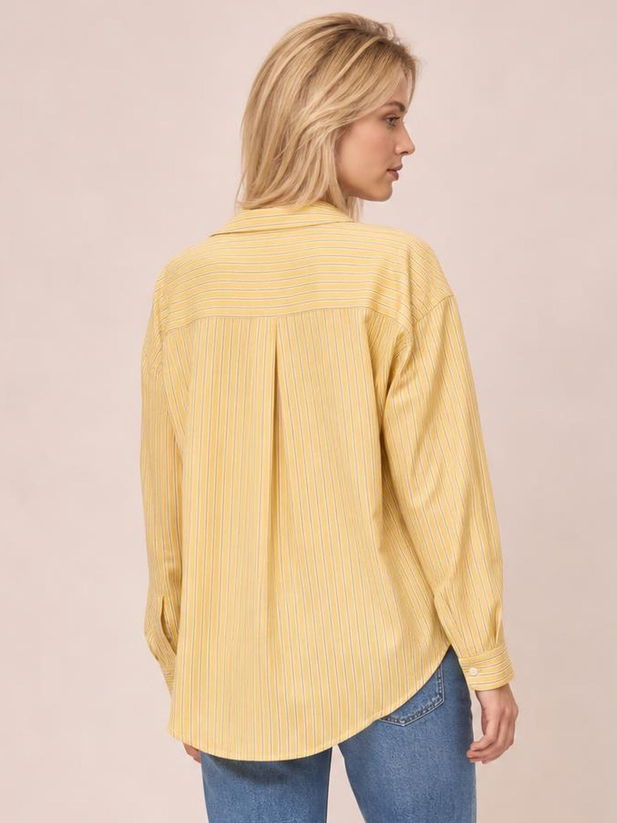 A model looks over her shoulder wearing a yellow striped button-up long sleeve shirt with a relaxed silhouette, curved hem, and structured back yoke.
