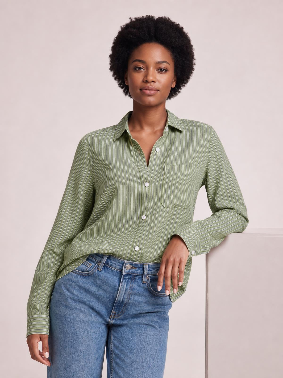 Model poses in a green striped button-up long-sleeve shirt with a collared neckline, front buttons, buttoned chest pocket, and relaxed silhouette.