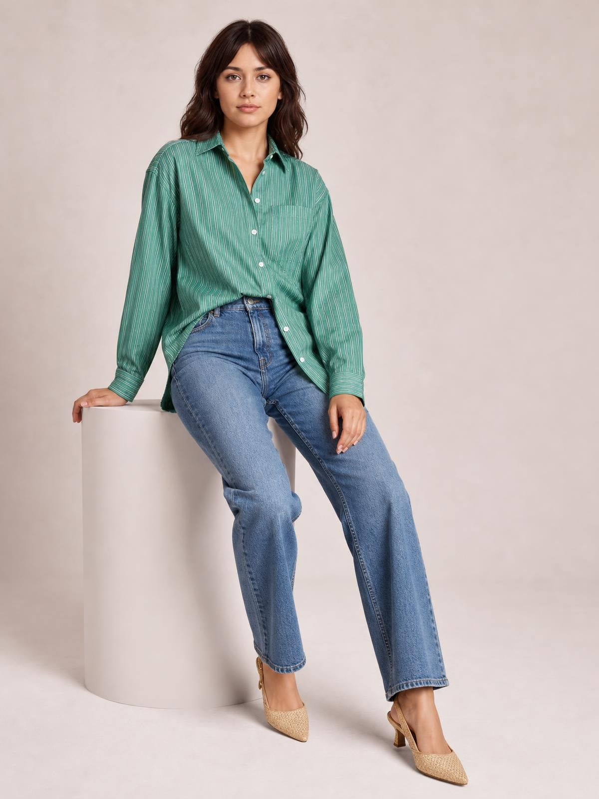 A model sits casually in a green striped button-up long sleeve shirt with a collared neckline, front buttons, and chest pocket.