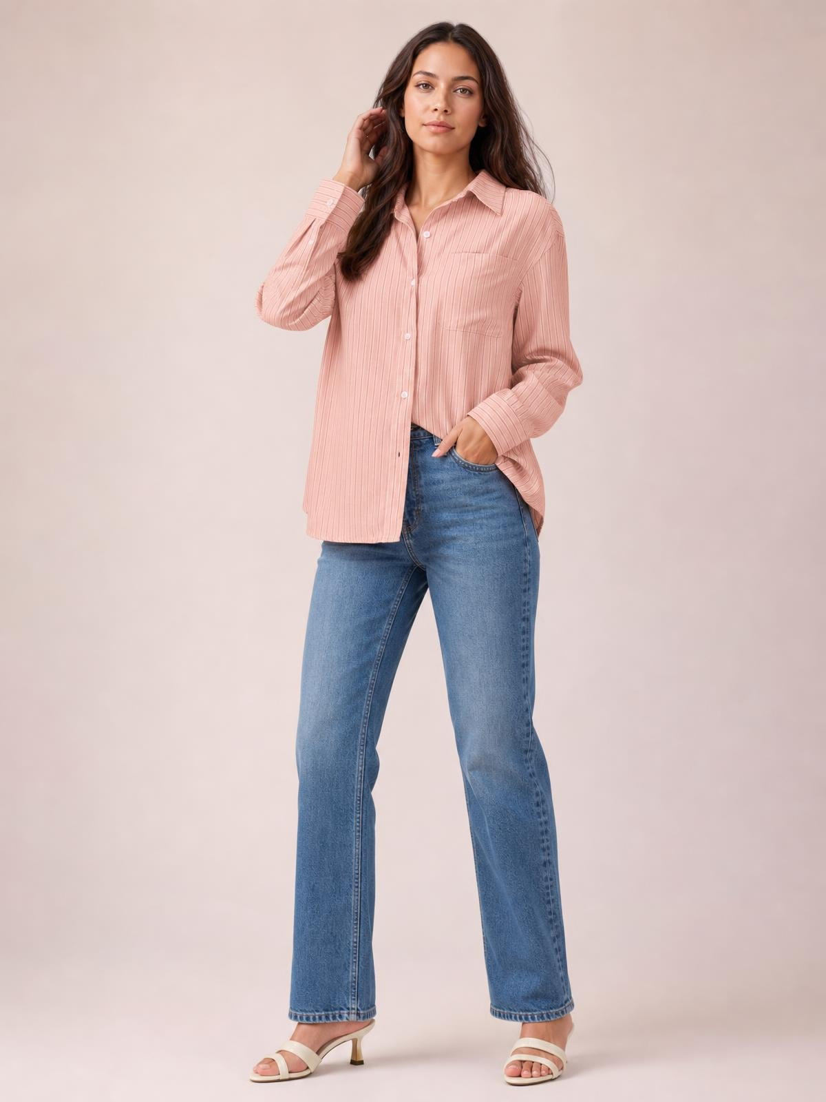 Model poses in a blush pink striped button-up long-sleeve shirt with a collared neckline, chest pocket, button closure, and relaxed straight silhouette.