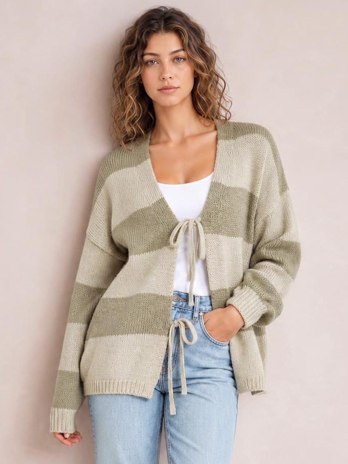 Model wearing a relaxed striped color block sweater cardigan in sage green and cream, with a V-neck, tie front, long sleeves, and ribbed cuffs and hem.