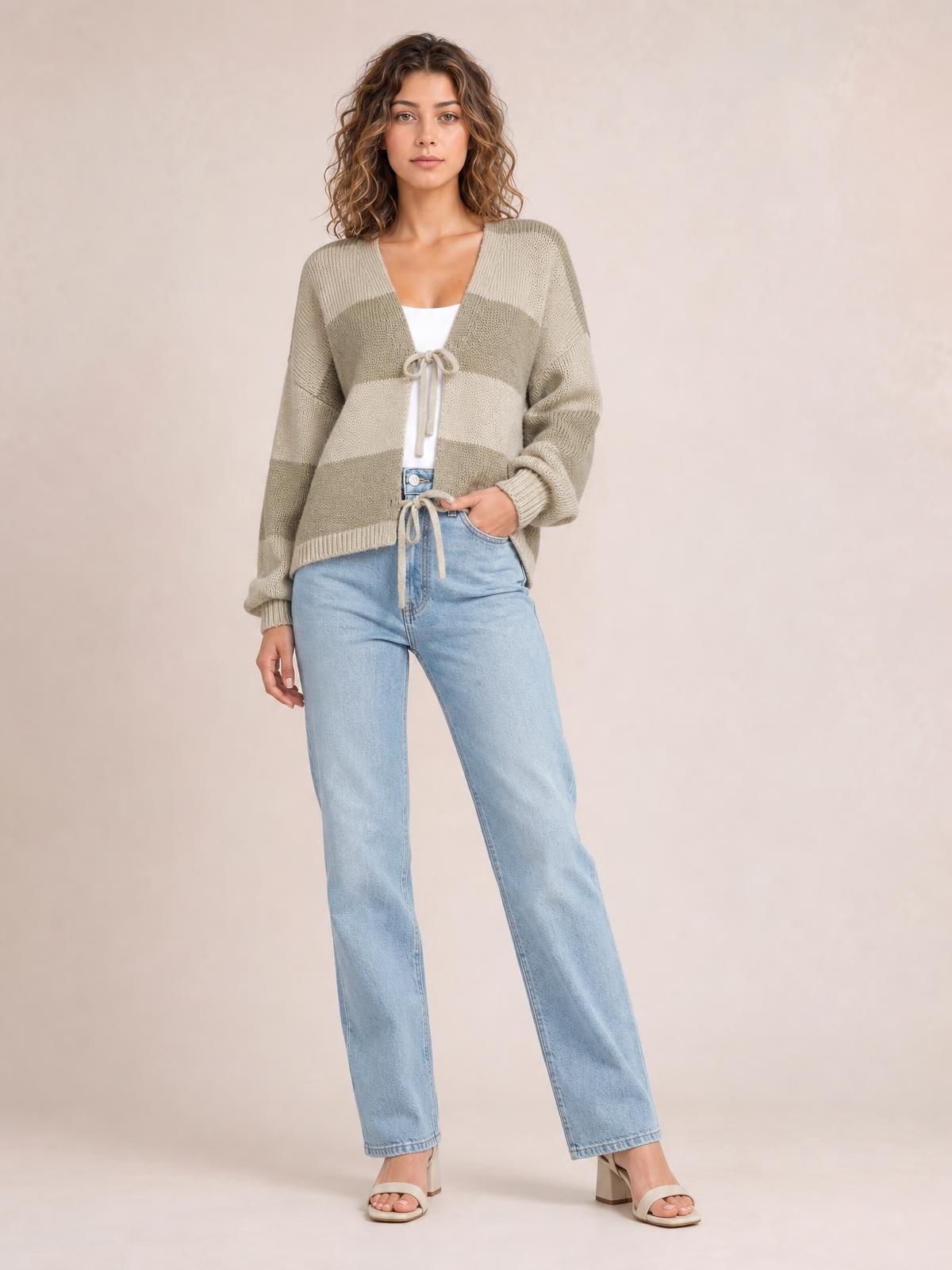 A model stands in a striped color block sweater cardigan with a V-neck, tie front, long sleeves, and relaxed silhouette in beige and taupe.